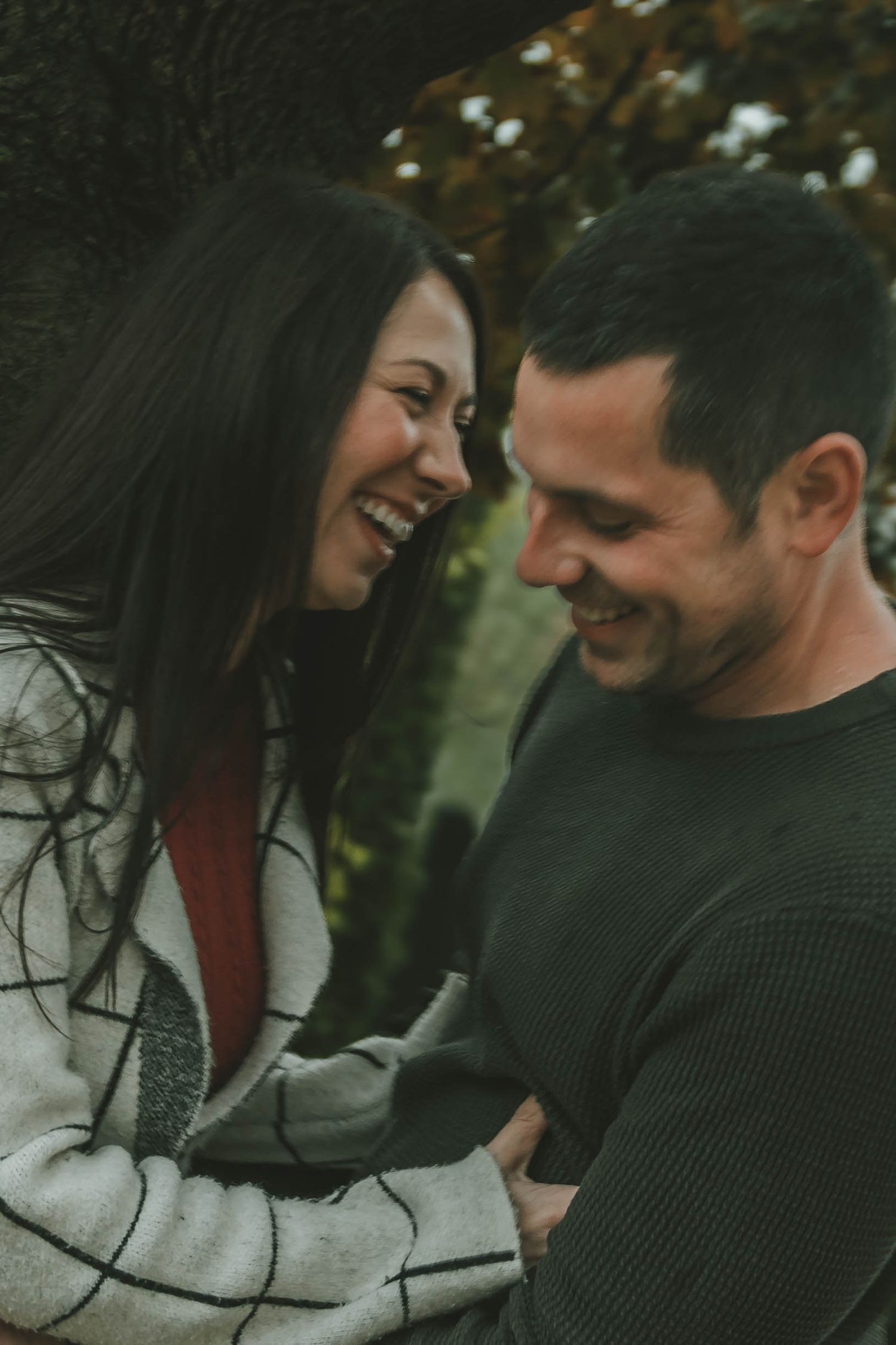 Two people share tender moments together while sitting outdoors on an autumn day with blurred background.