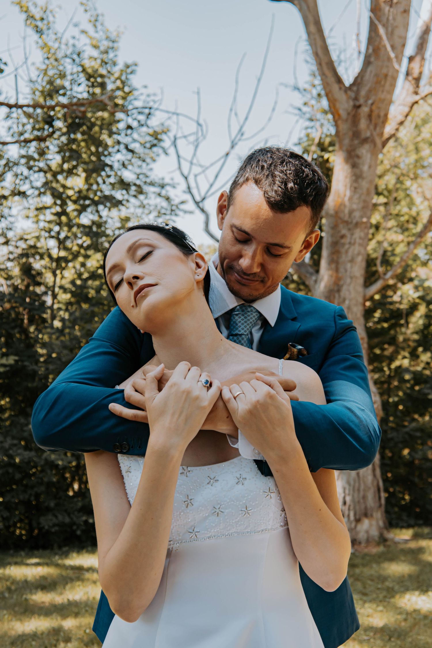 A romantic embrace between newlyweds in a sunny garden setting.