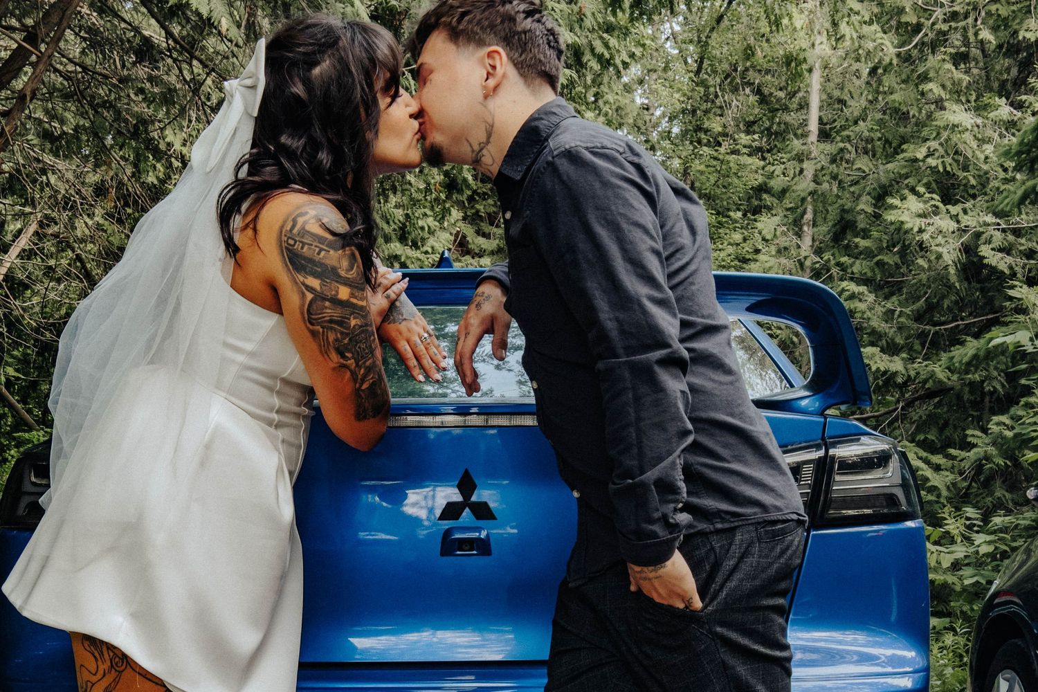 A series of intimate moments captured against a blue car in a wooded outdoor setting.