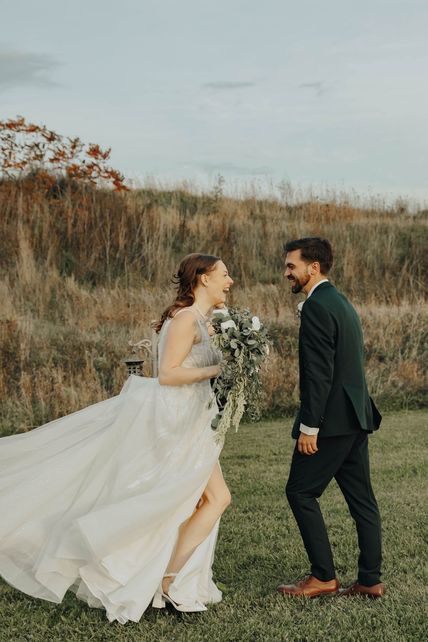 A wedding couple shares playful moments in a rustic outdoor setting with tall grass and autumn colors.