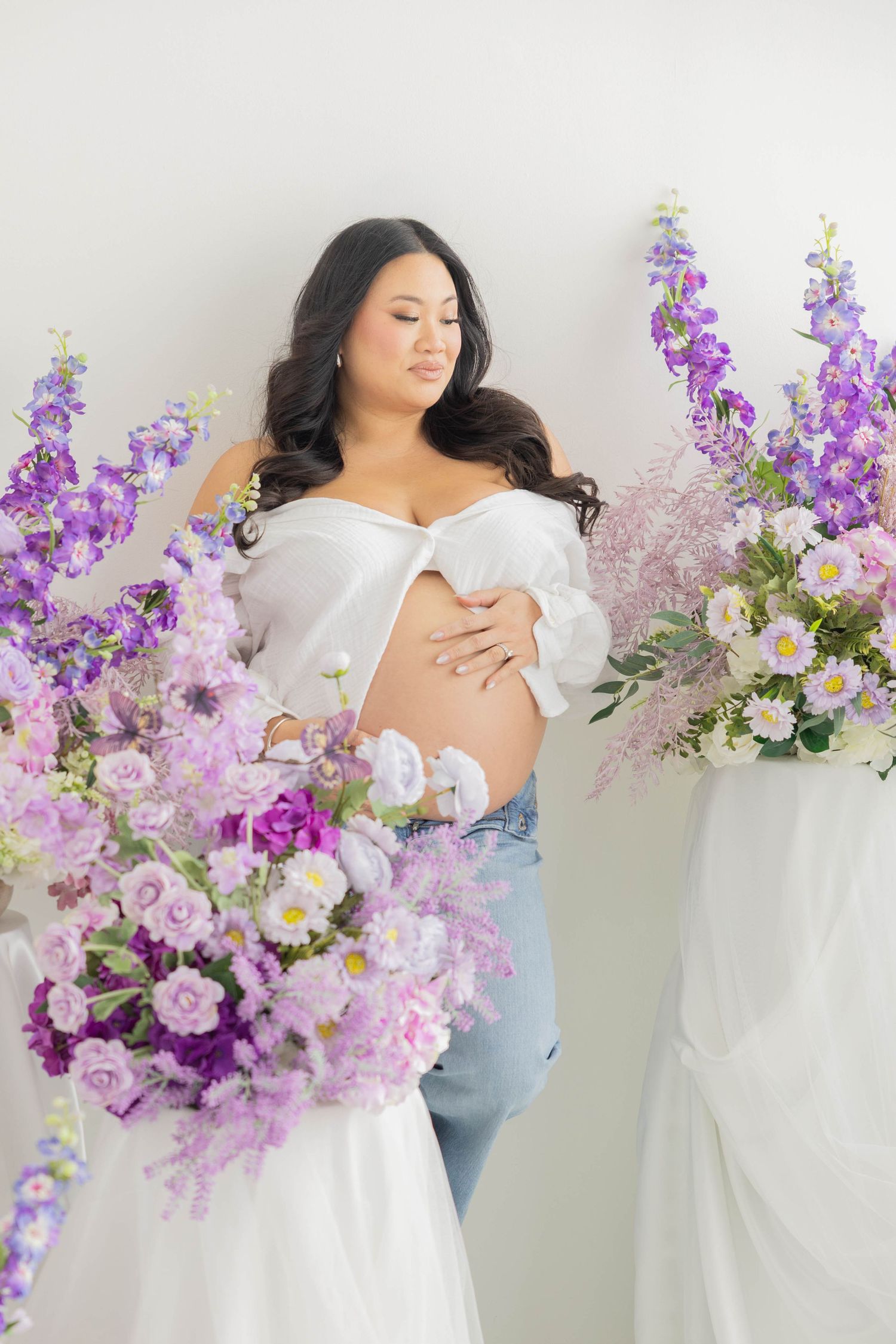 Dreamy boudoir photoshoot with delicate purple and pink florals decorating a minimalist white studio space.
