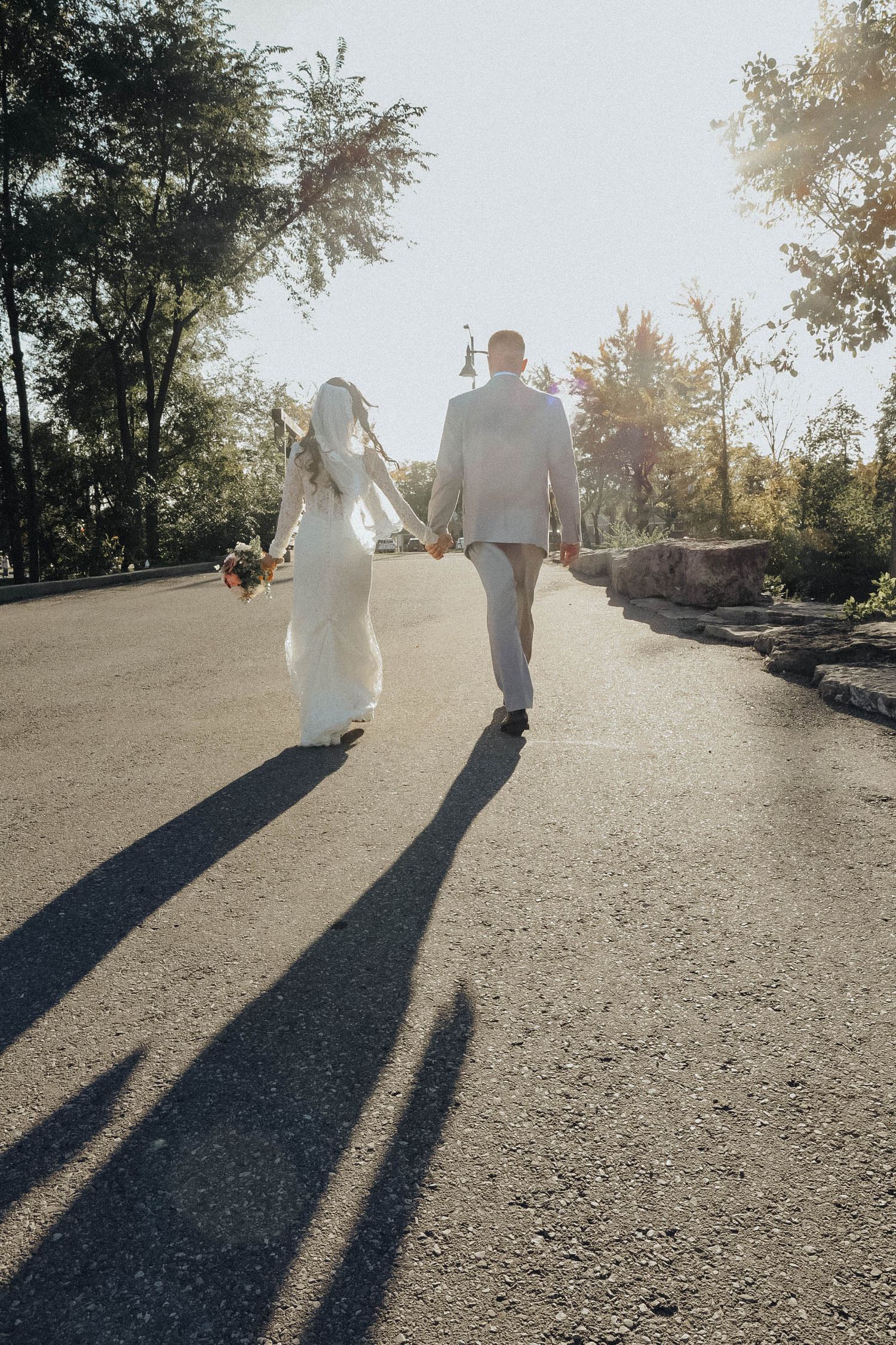 Long shadows of a couple in white clothing walking down a sunlit path at sunset.