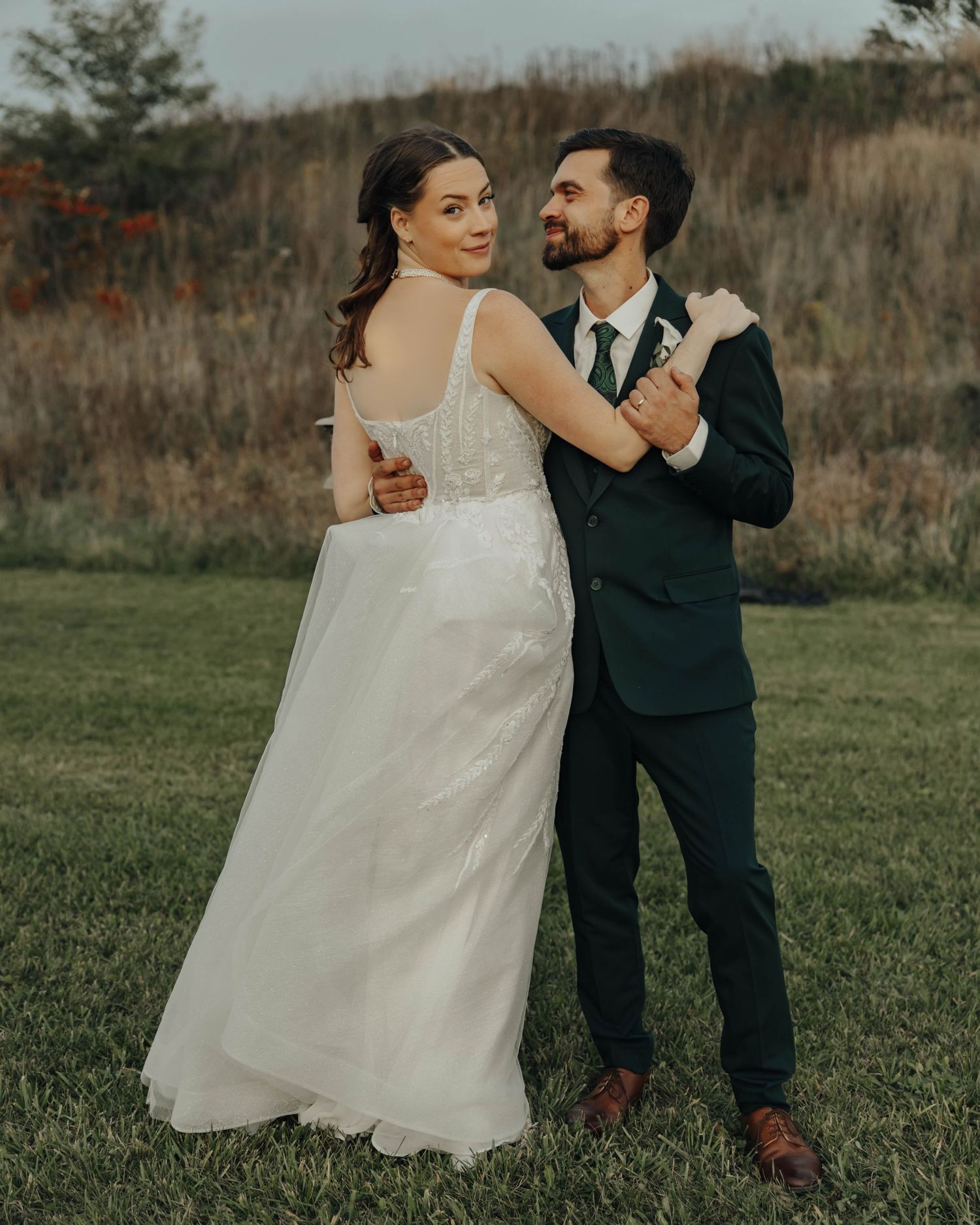 A couple shares a joyful moment together in an outdoor field during their wedding photoshoot.