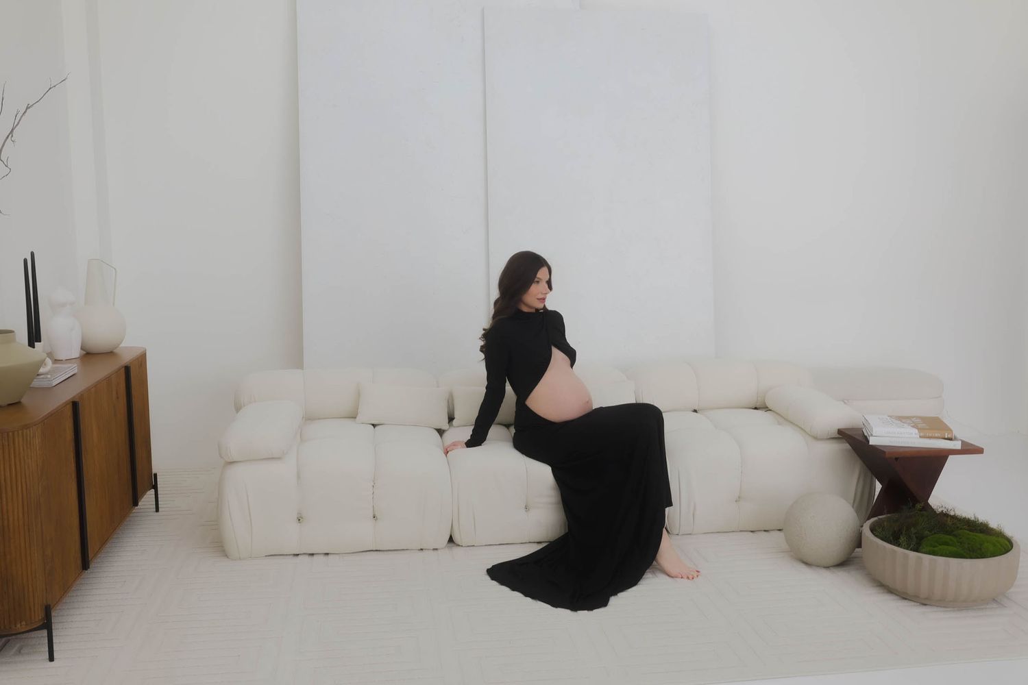 A minimalist maternity photo shoot in an all-white room with modern furniture.