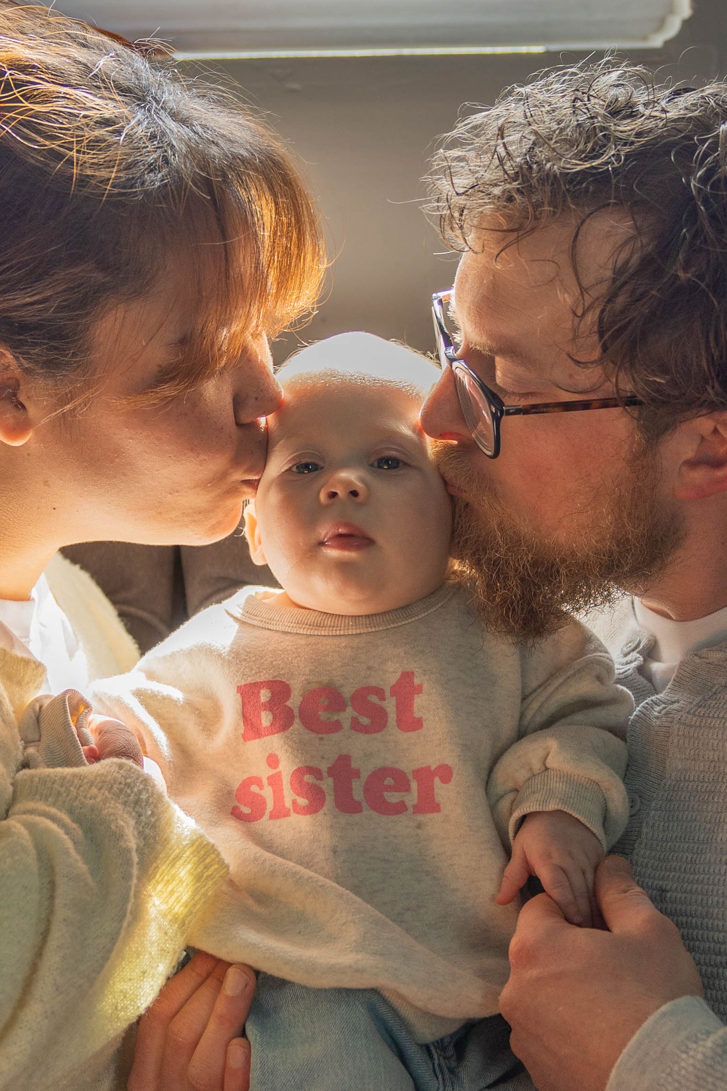 A tender moment captured in warm sunlight shows a parent sharing affectionate moments with a young child wearing a sweater.