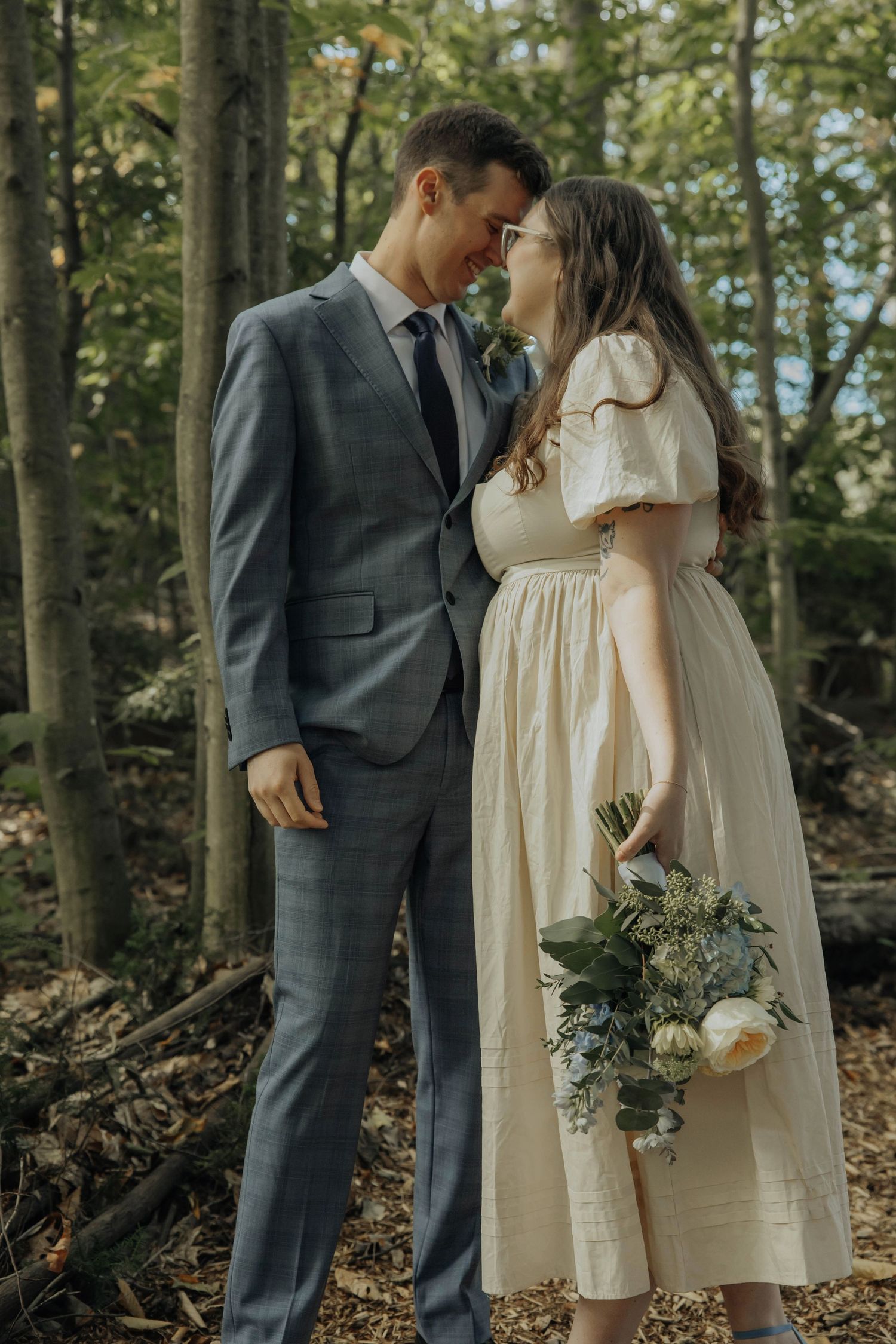 A romantic couple in formal attire shares intimate moments in a wooded forest setting with natural lighting.