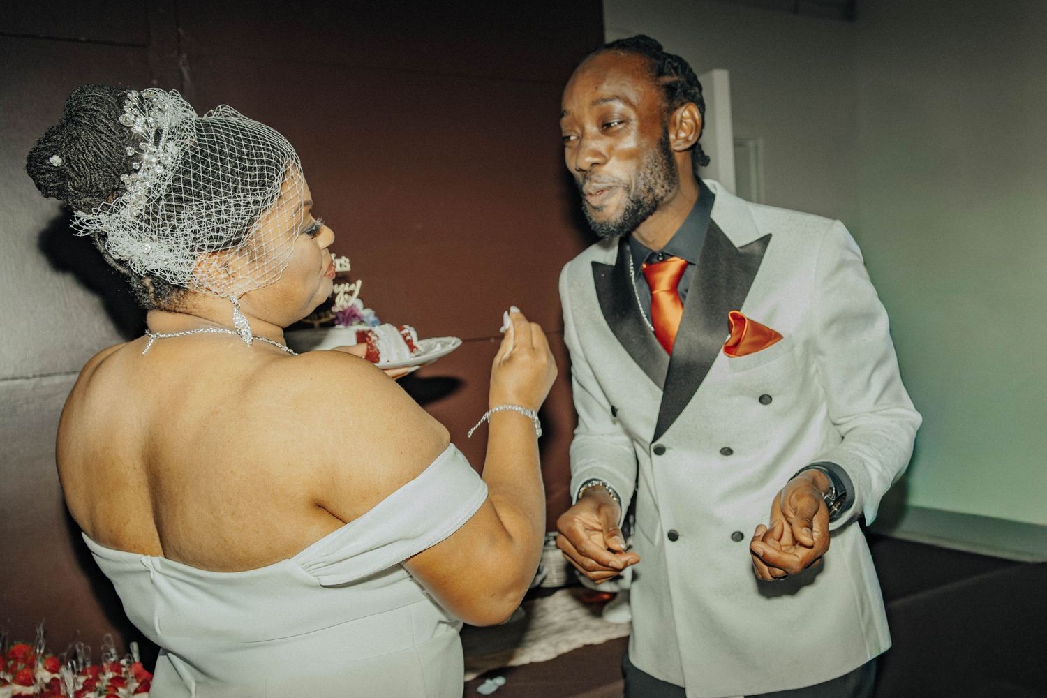 A couple dances together at a social event, with the woman wearing an off-shoulder dress and the man in a light-colored suit.