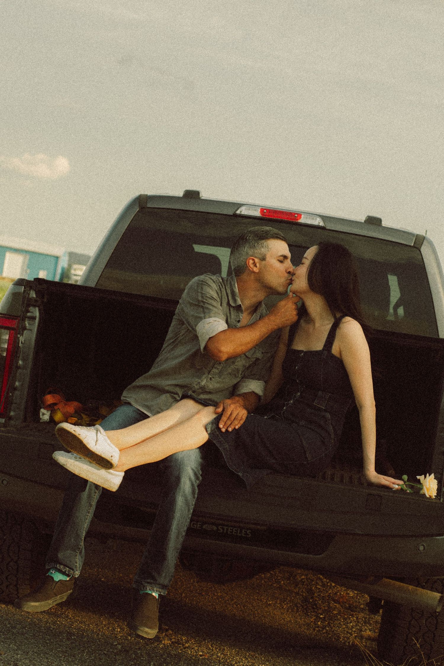 Romantic couple kissing while sitting on a truck tailgate at golden hour.