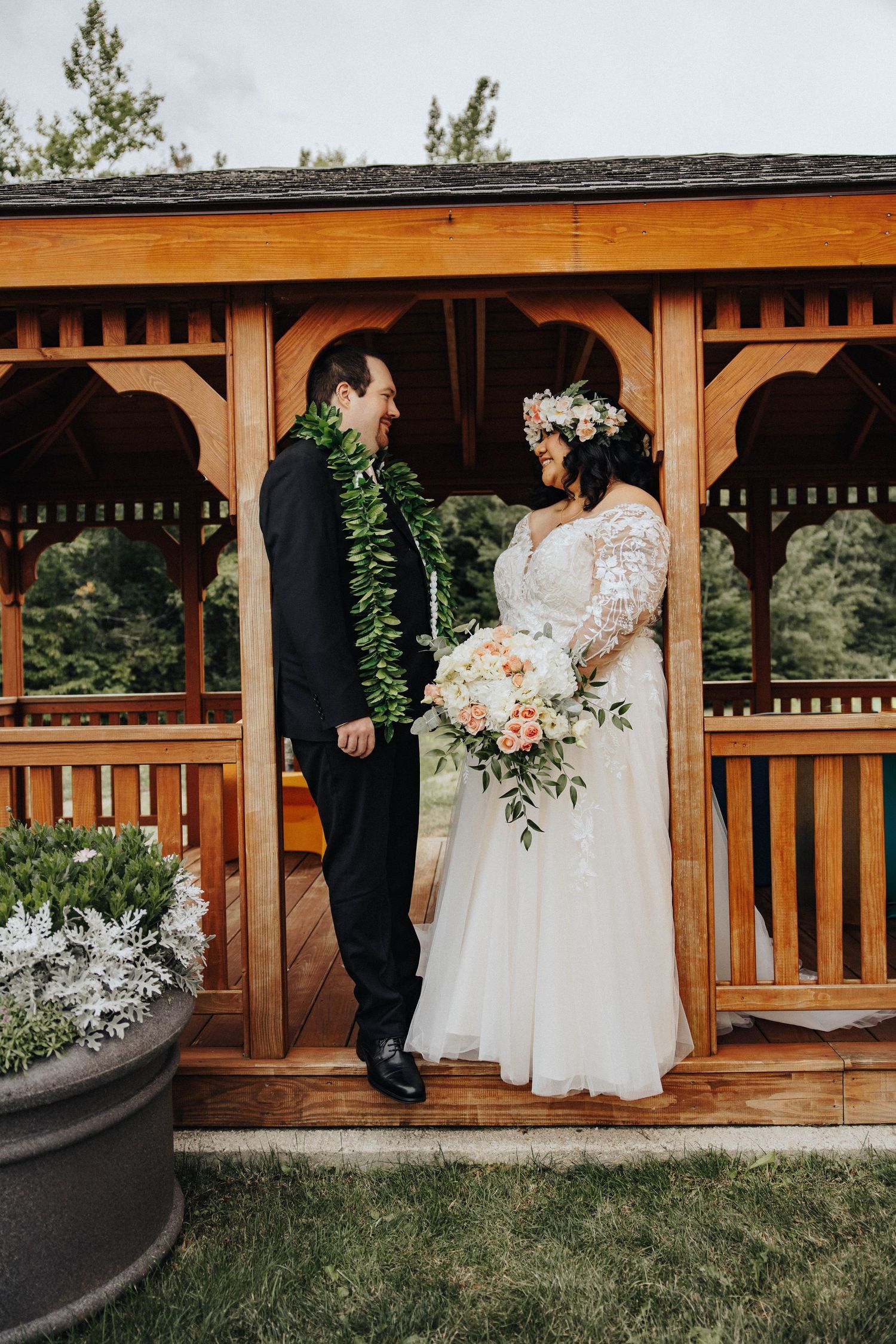 Wedding couple shares intimate moments under a rustic wooden gazebo surrounded by greenery.