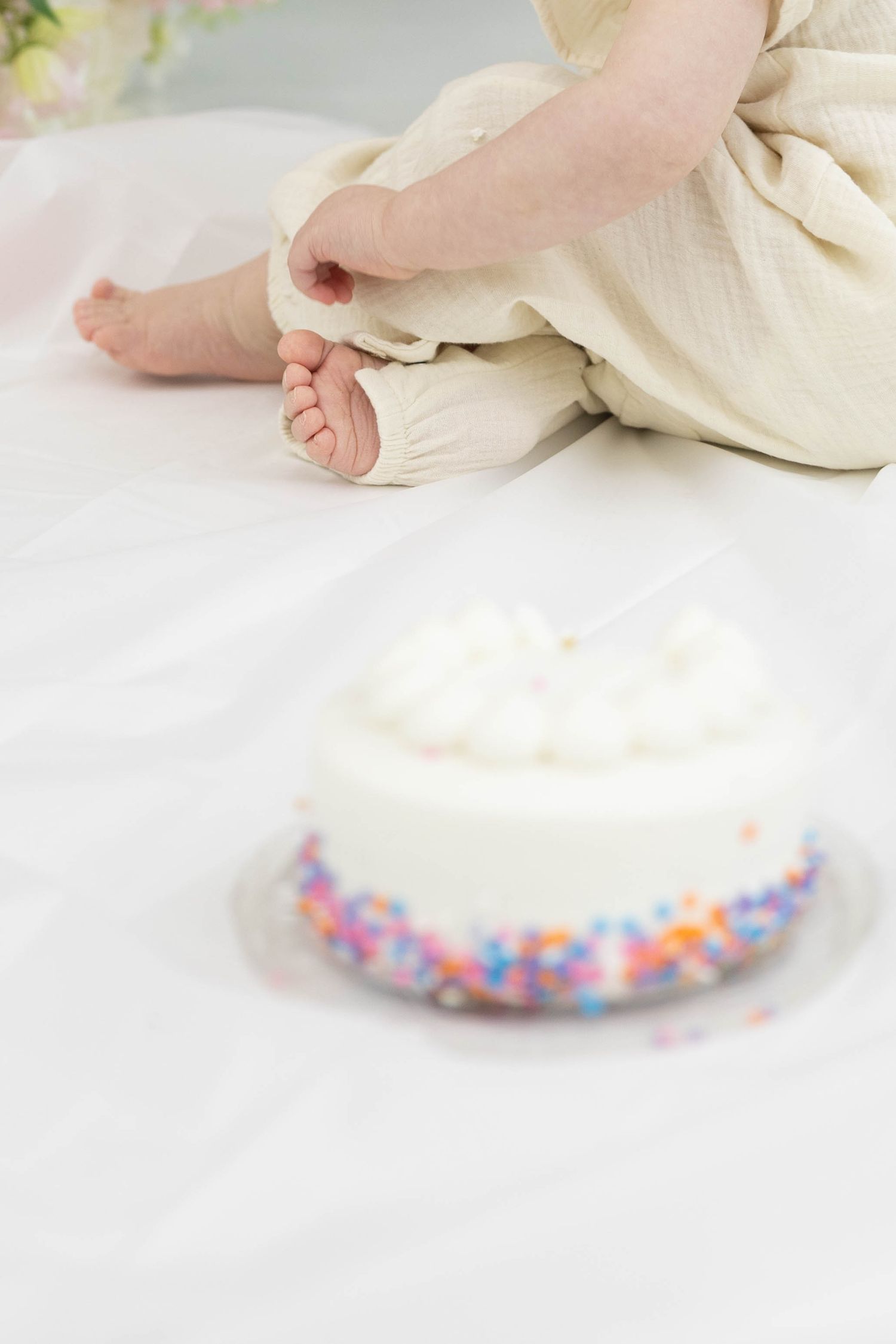 Small baby feet in cream-colored clothing resting near a plate decorated with colorful sprinkles on a white surface.