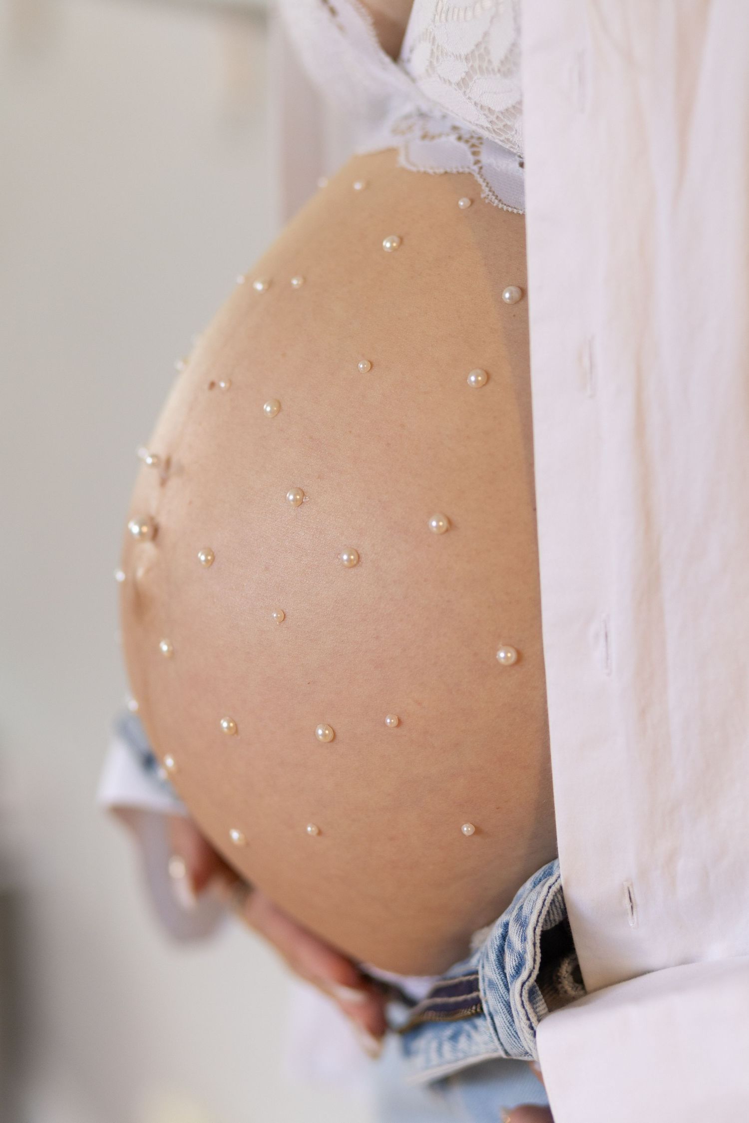 Close-up of pregnant belly decorated with pearl stickers, worn with lace bra and denim jeans.