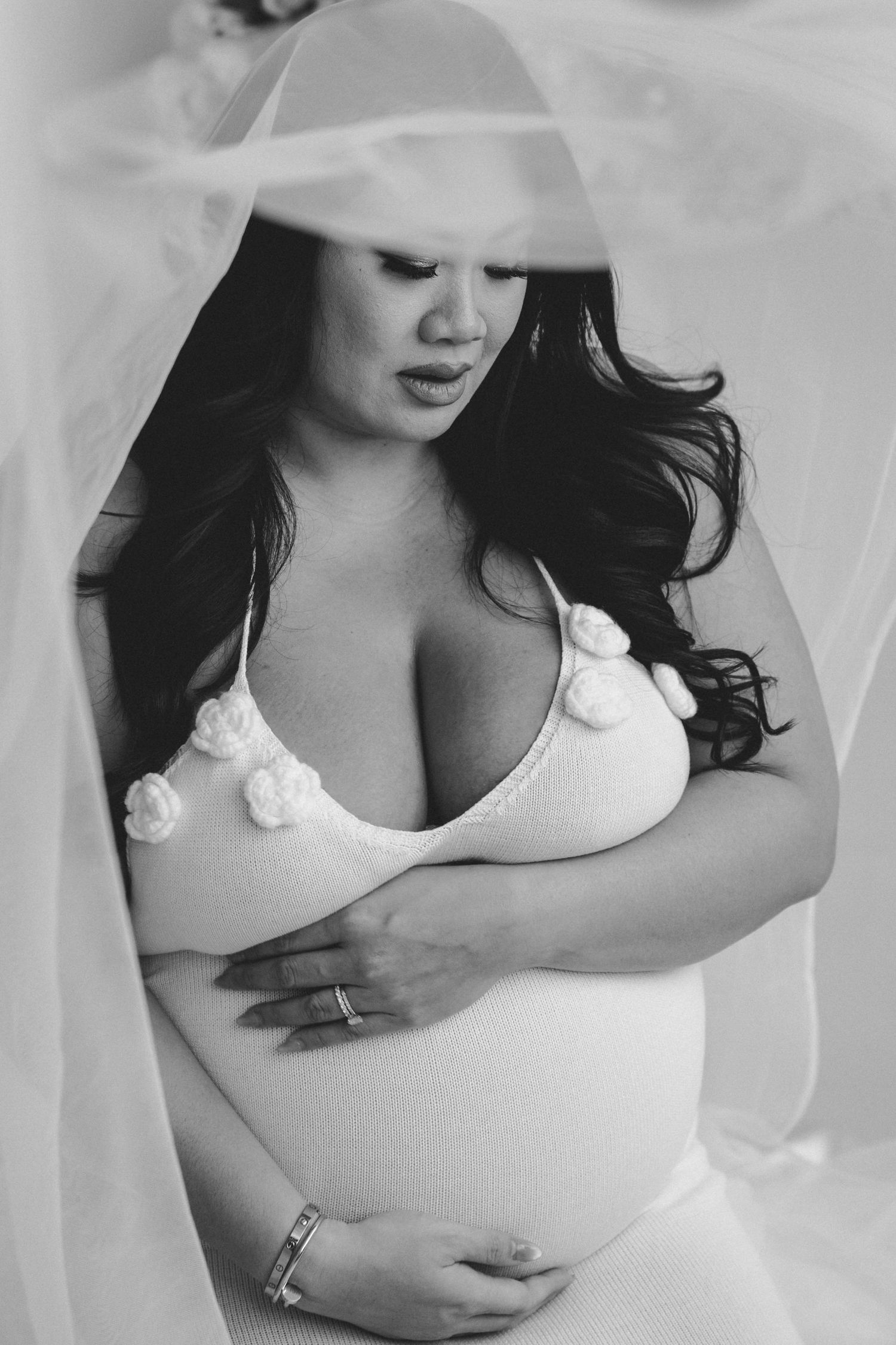 Black and white maternity photo with soft tulle veil and white top creating an elegant silhouette.