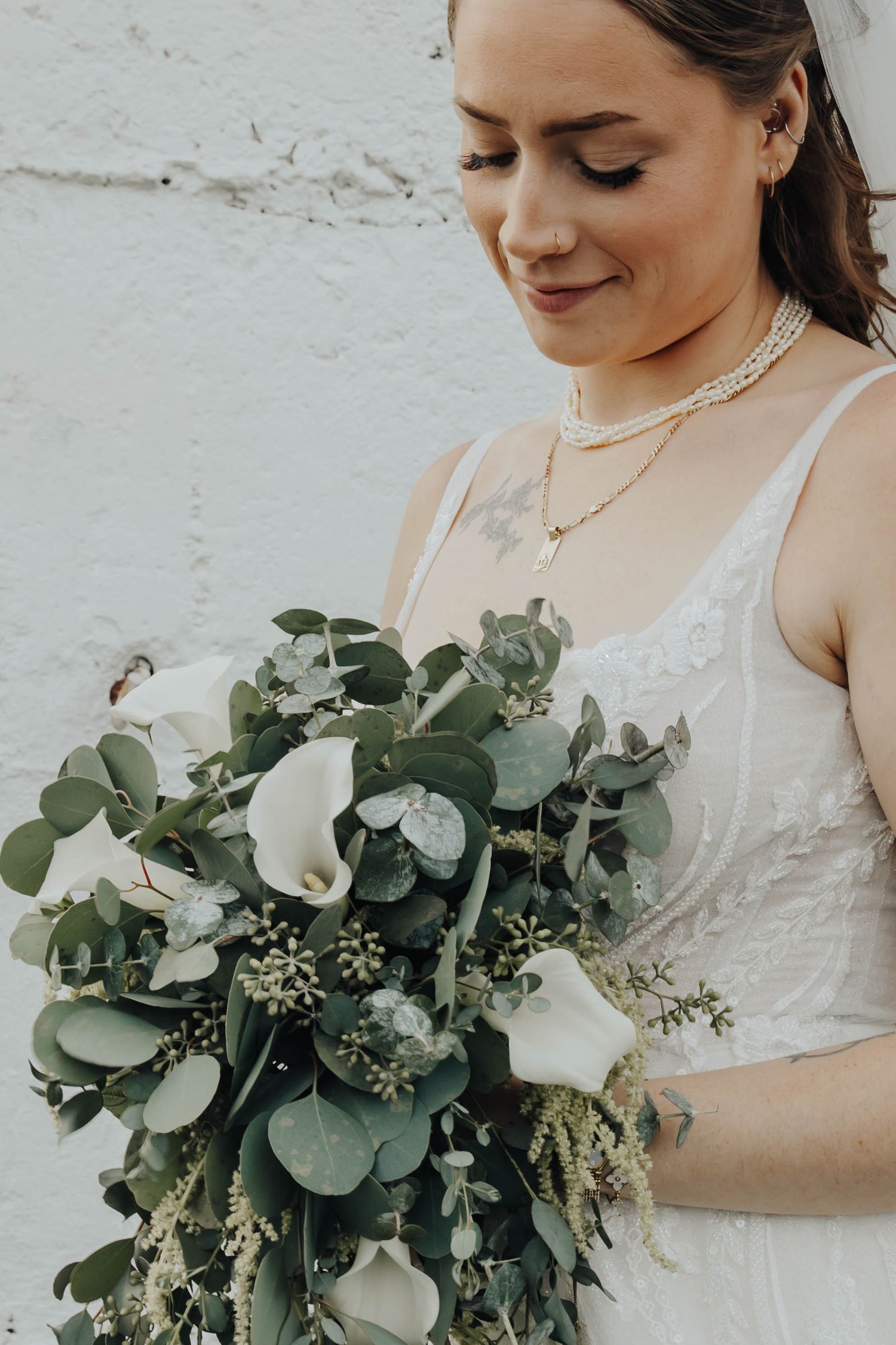 Elegant bridal bouquet featuring white calla lilies and lush eucalyptus greenery against a white wall.