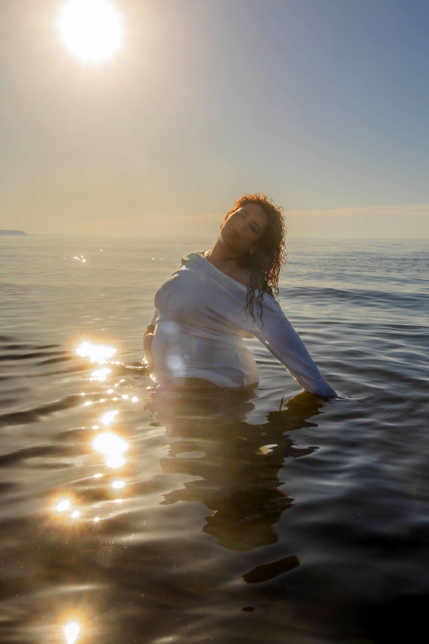 Person in white floating in ocean water during golden hour with sun reflections on waves.