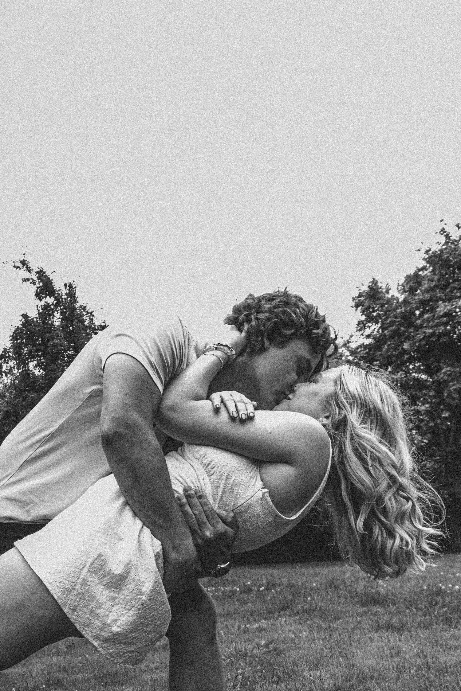 Black and white artistic photo of couple embracing in an outdoor setting.