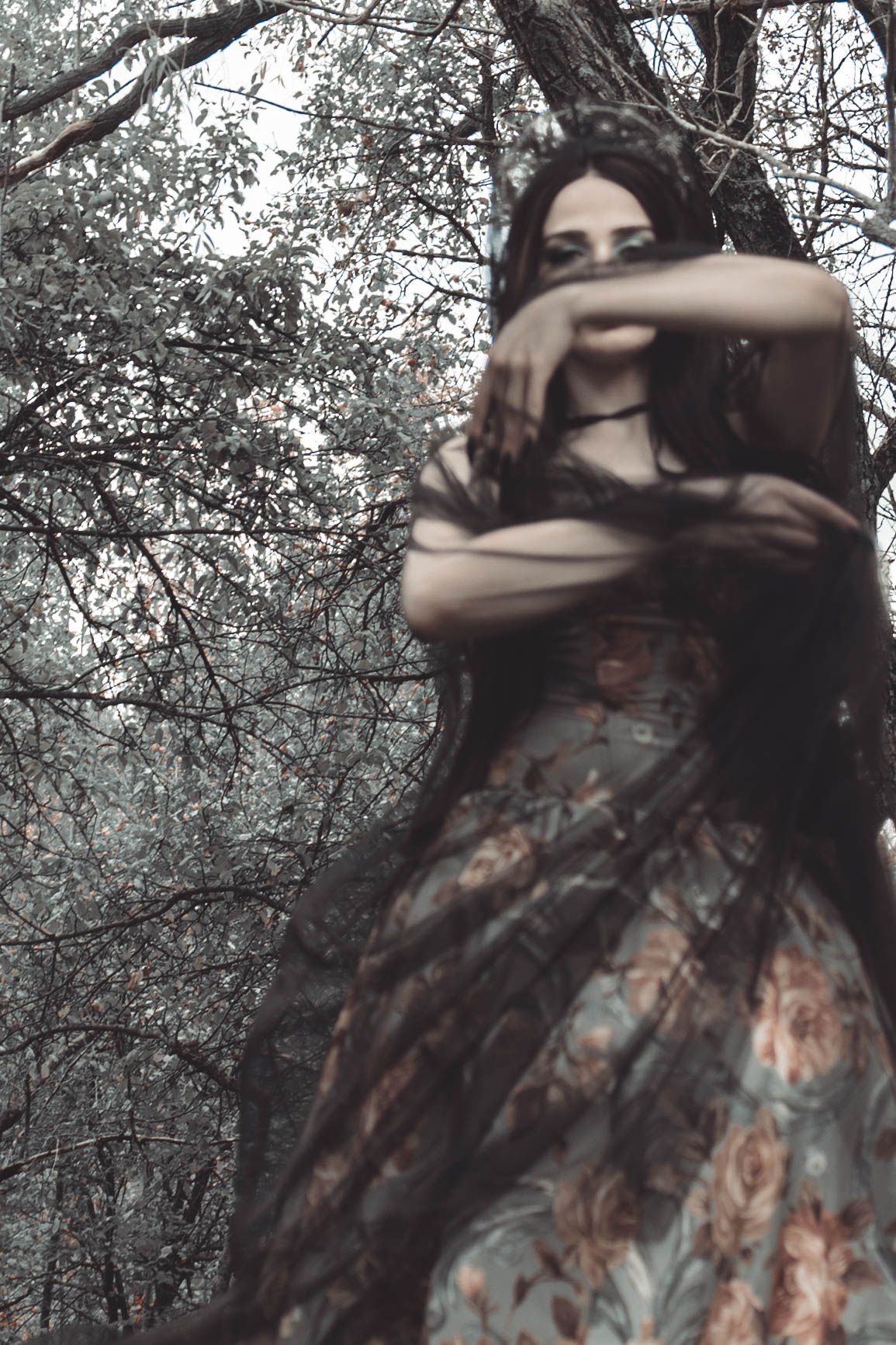 A figure in a floral dress moves through a moody forest setting creating a dreamy, ethereal atmosphere.
