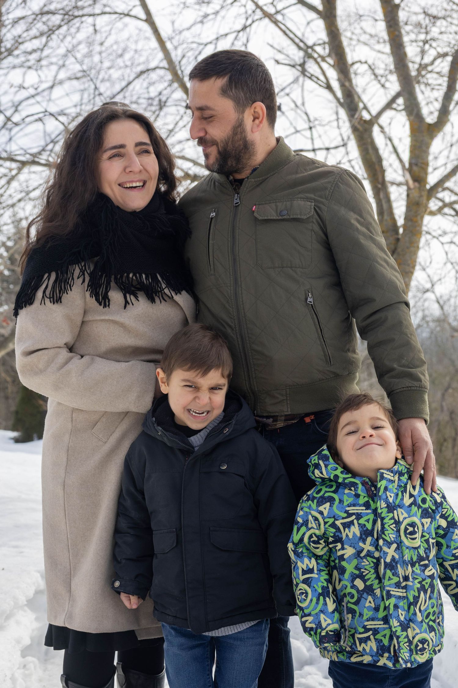 Family enjoying a winter day together in the snow wearing warm coats and sharing laughs and hugs.