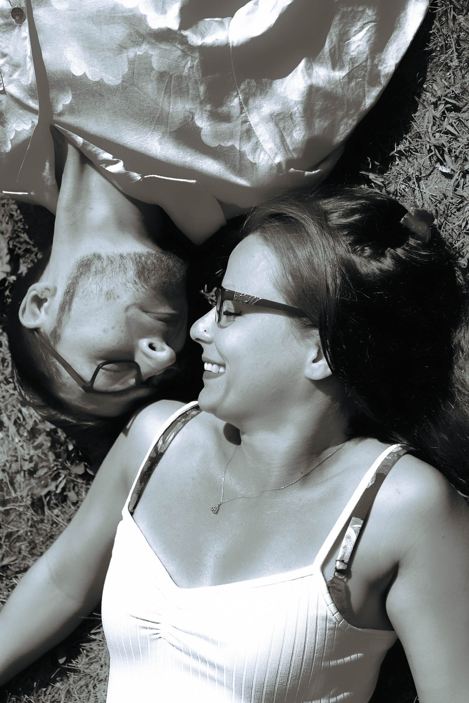 A black and white photo of a couple lying together and smiling on the ground.