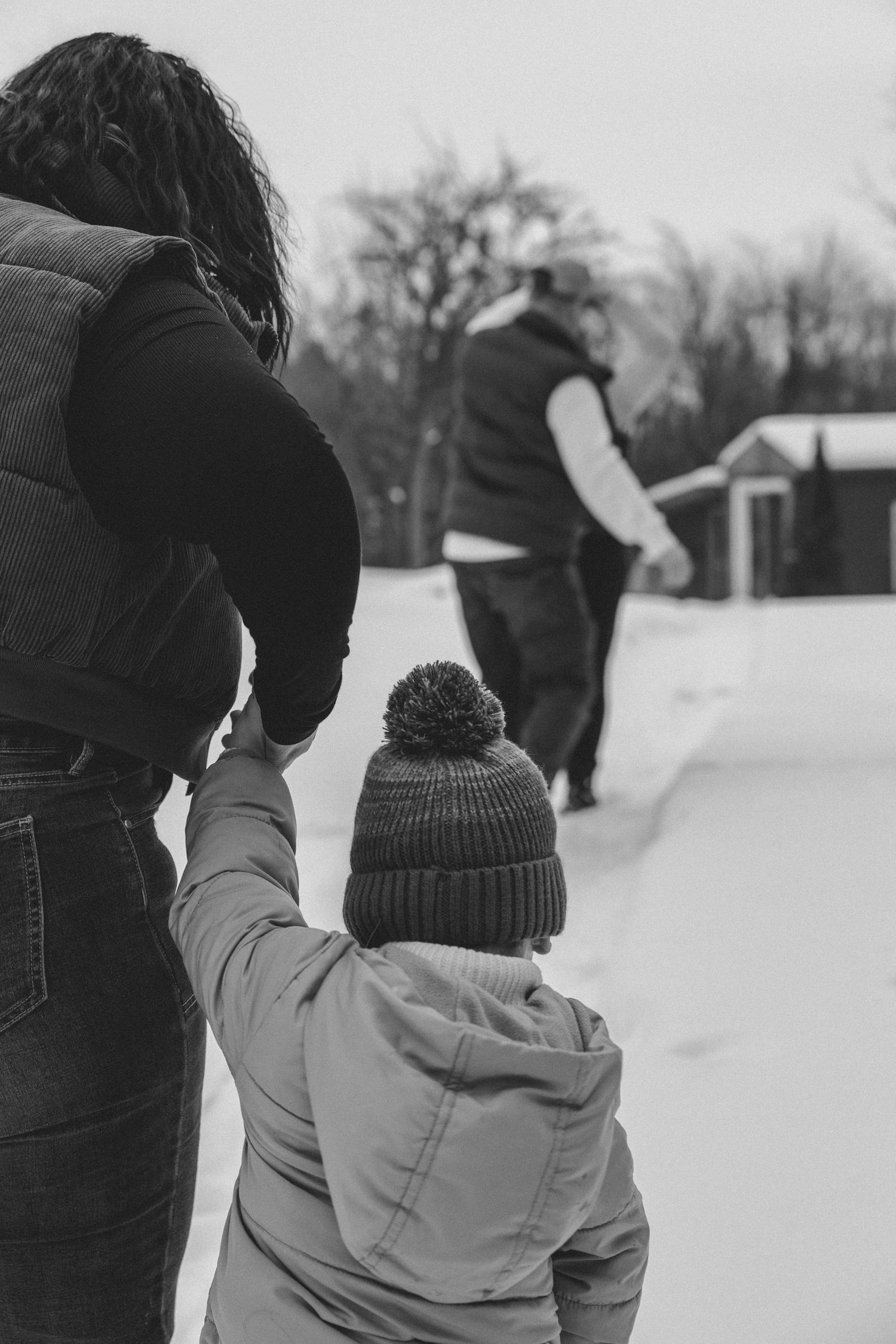 Black and white photo of a child in a winter hat with adults walking on a snowy path during winter.