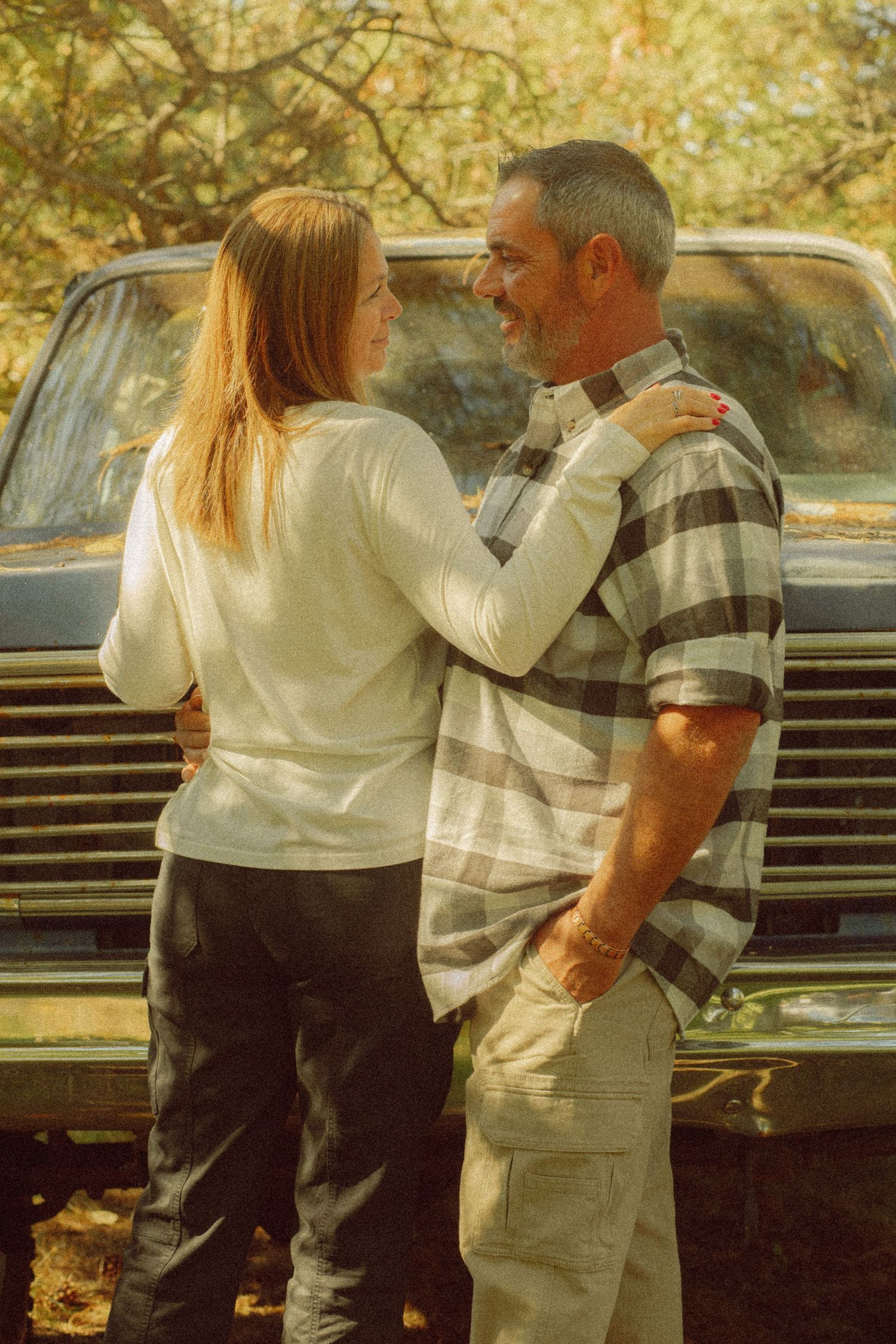 Couple embracing and smiling at each other in front of a vintage truck surrounded by autumn foliage.
