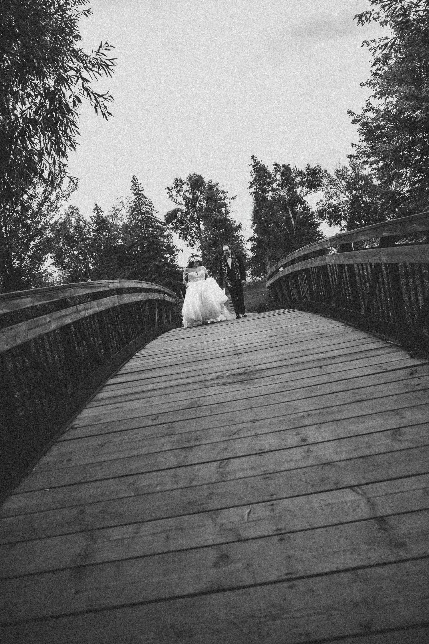 Black and white image of a curved wooden boardwalk through trees.