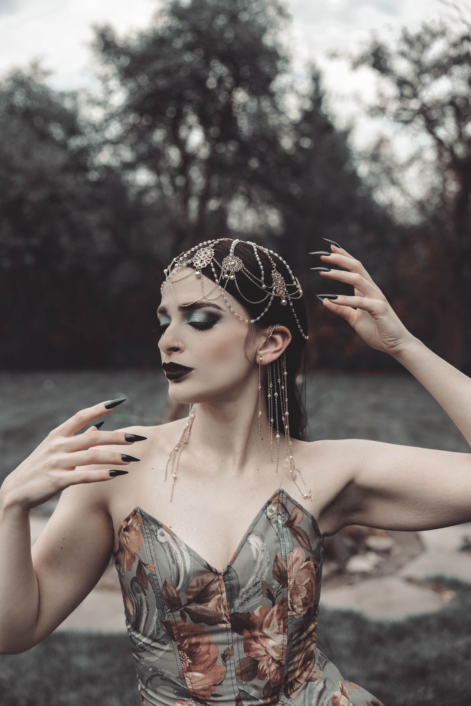 Artistic portrait showcasing dramatic makeup and jewelry in a desaturated outdoor setting.