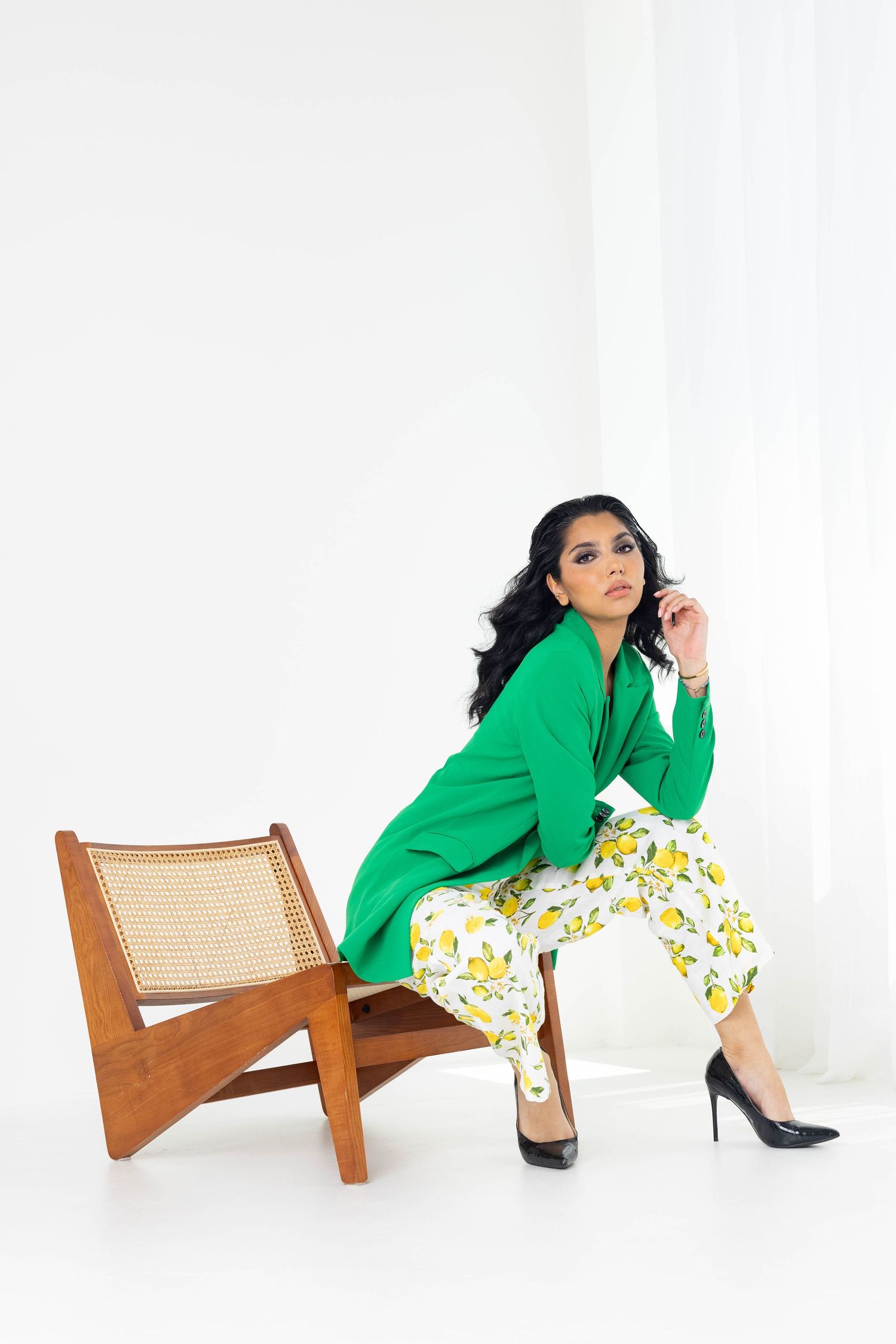 Model in vibrant green blazer and floral pants poses elegantly in a series of four stylish poses with a wooden chair.
