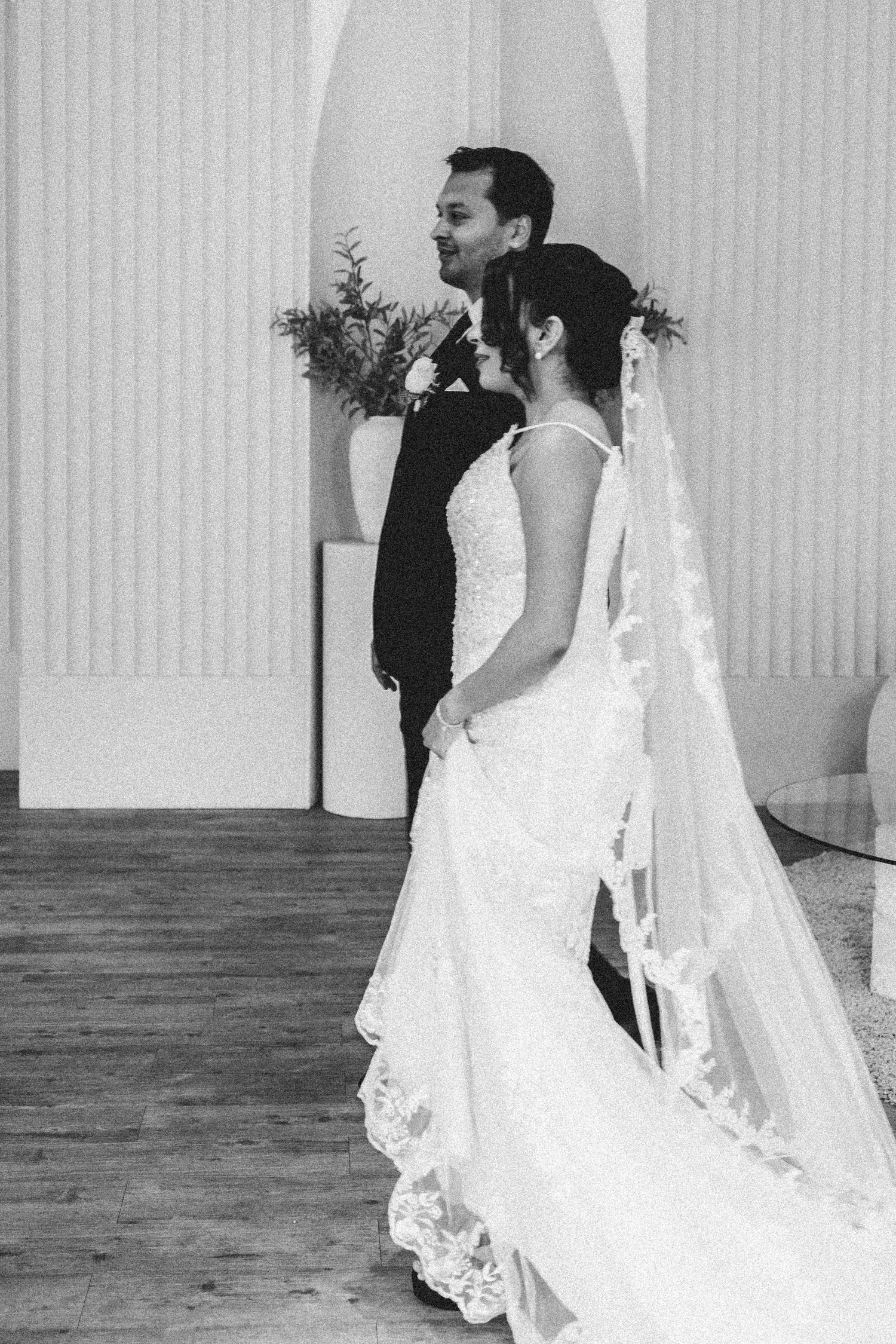 Black and white wedding photo showing a couple side by side at the altar, bride wearing lace veil and elegant white gown.