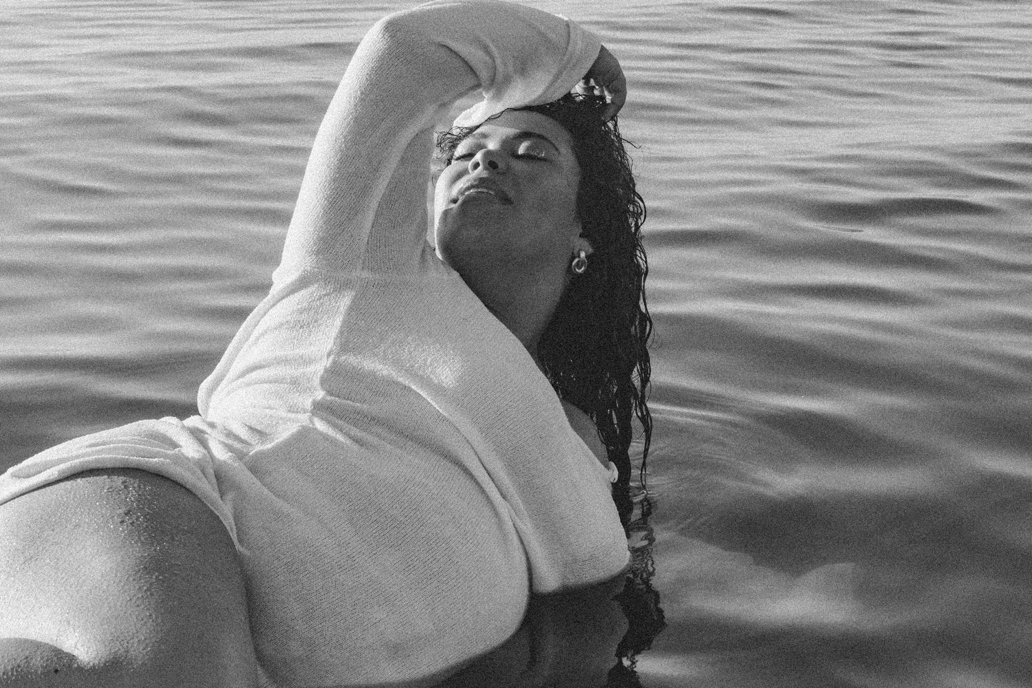 Figure in white clothing floating on back in dark ocean waters.