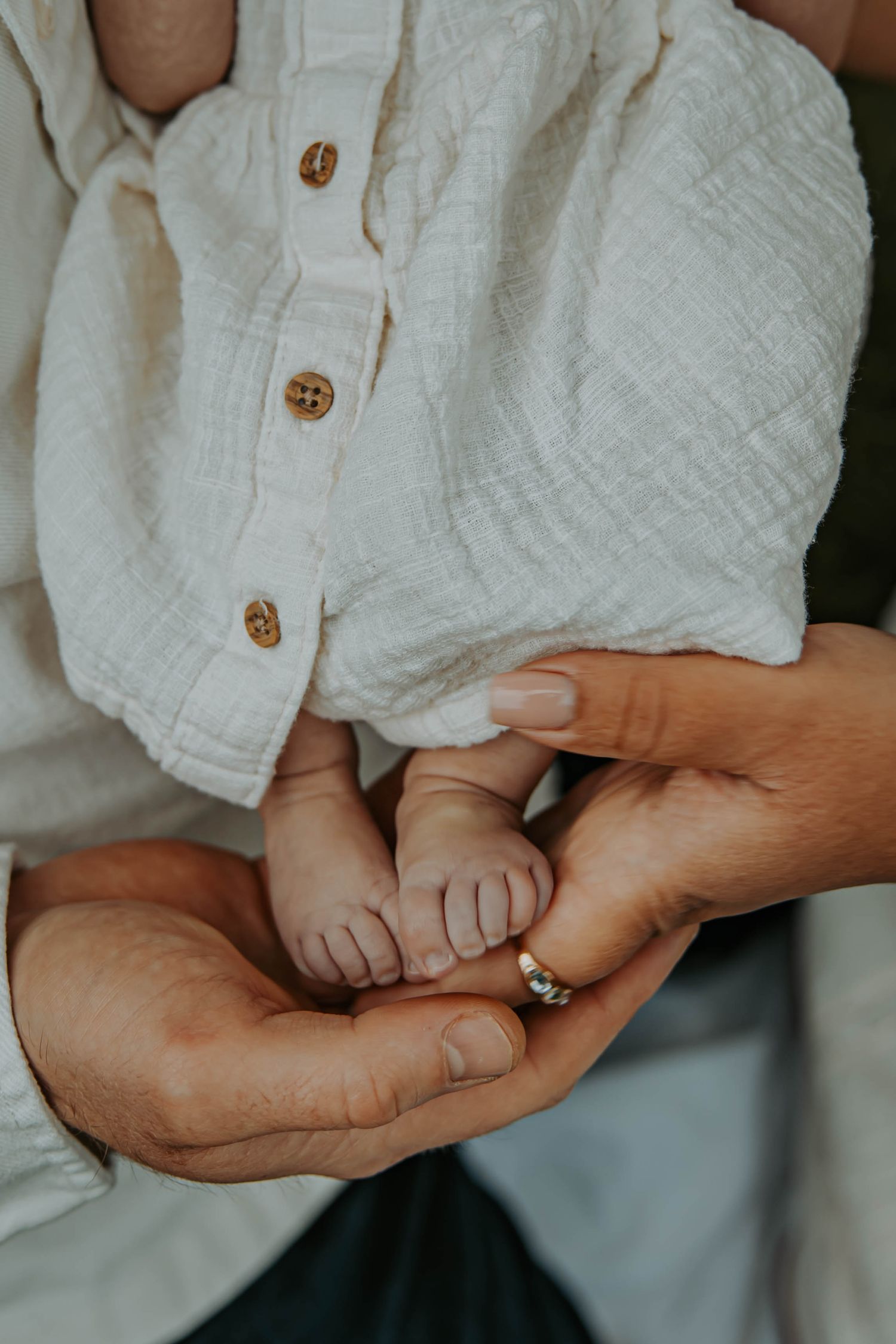 Close-up of adult hands gently cradling tiny baby feet against white fabric background.