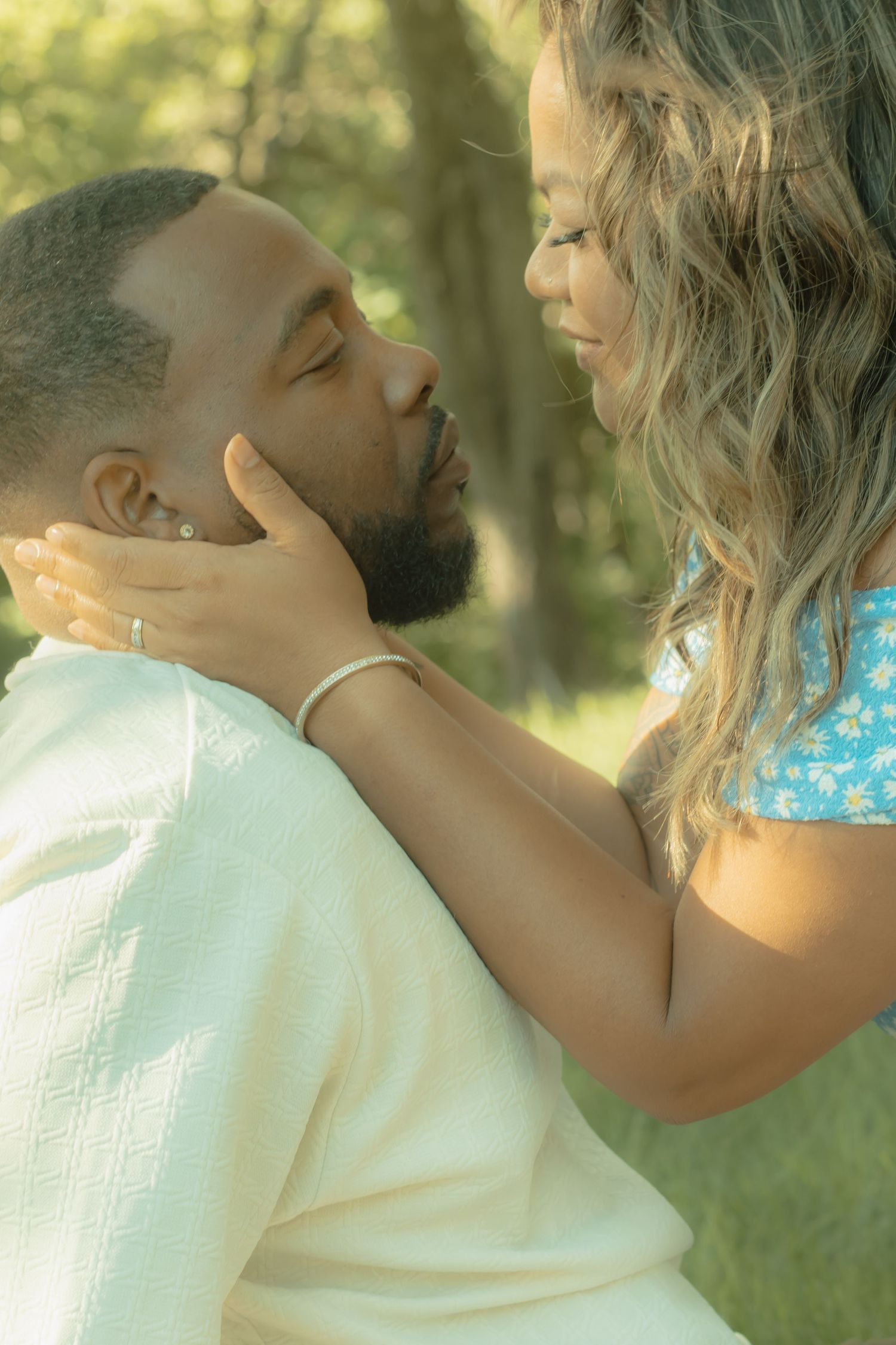A tender moment between a couple outdoors, woman gently holding mans face as they share an intimate close embrace.