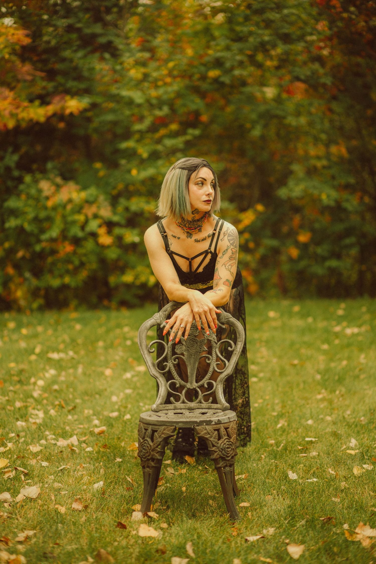 Tattooed woman with gray hair poses on vintage iron chair in autumn garden wearing black lingerie.