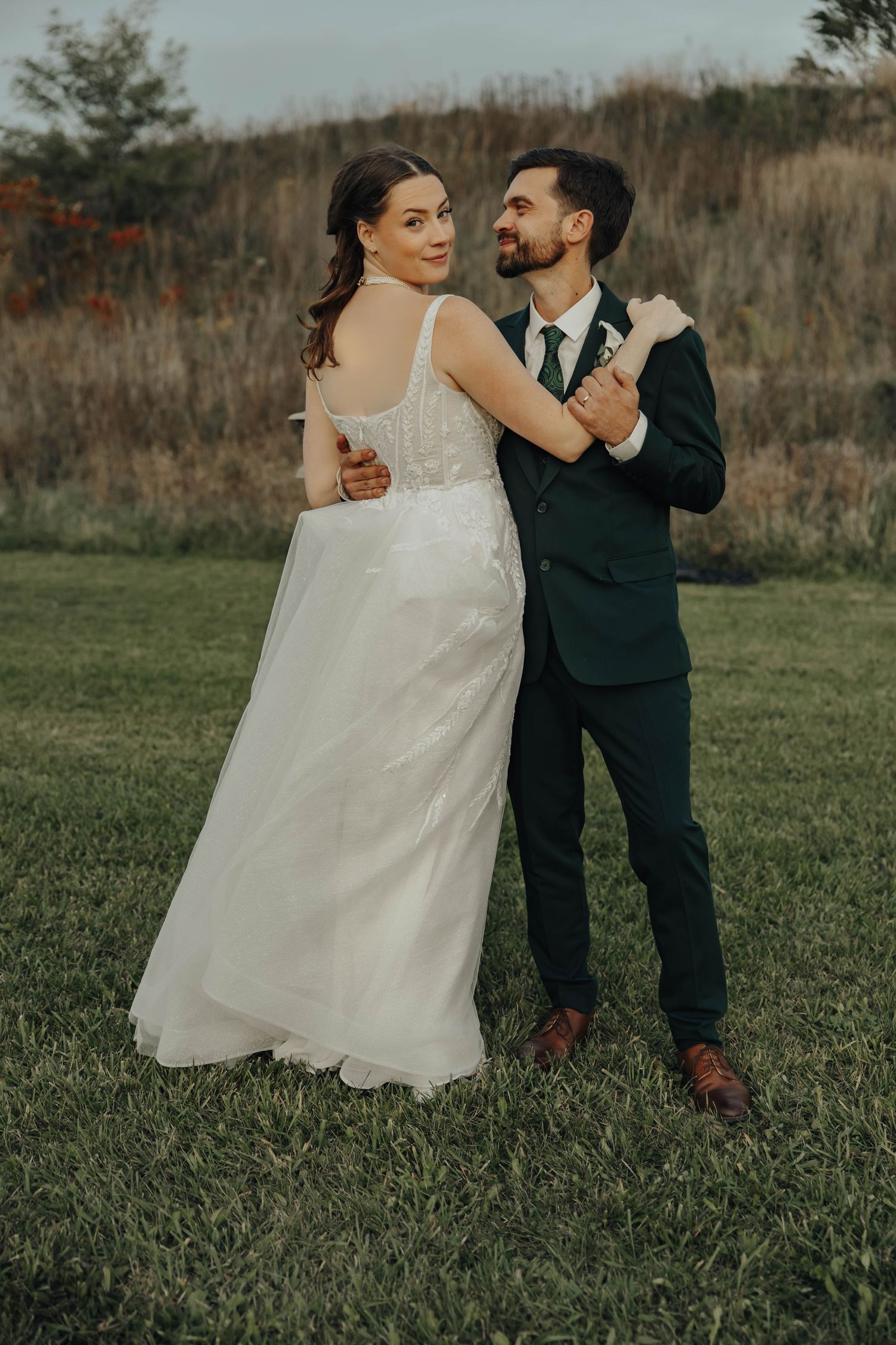 Couple shares a joyful dance moment on their wedding day in an outdoor field setting.