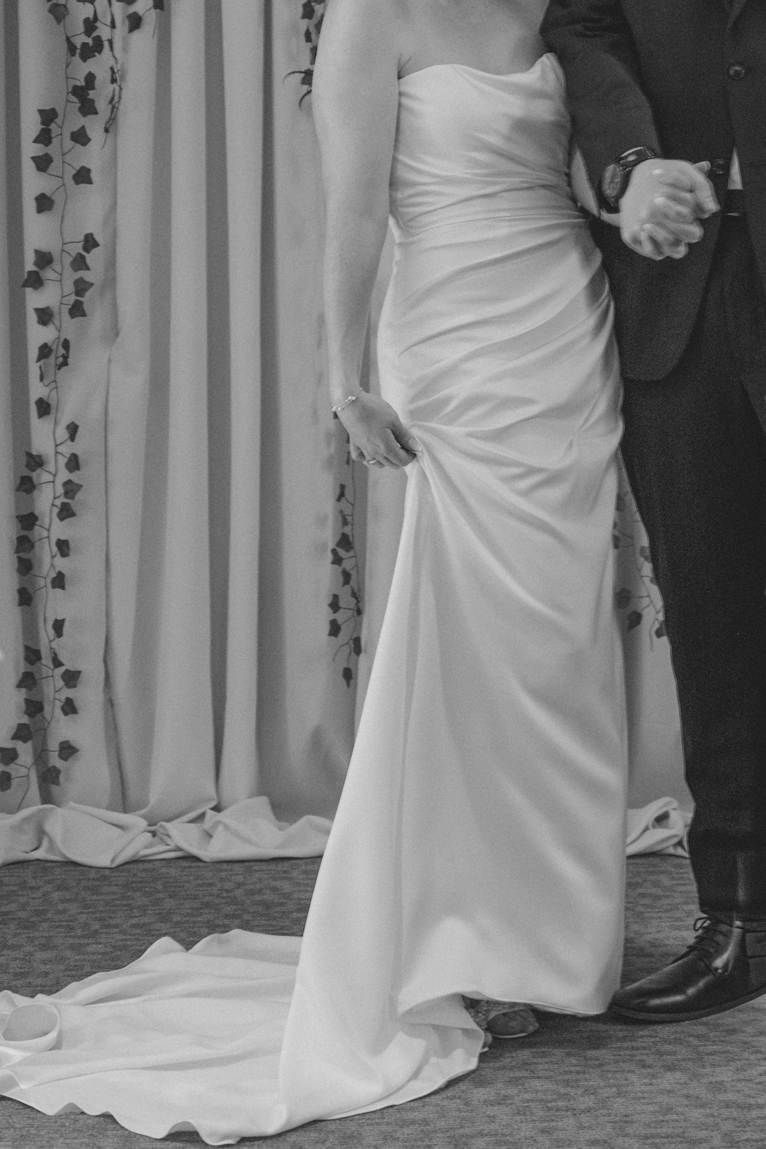 Black and white photo of a bride in a strapless gown and groom in a suit holding hands at their wedding ceremony.