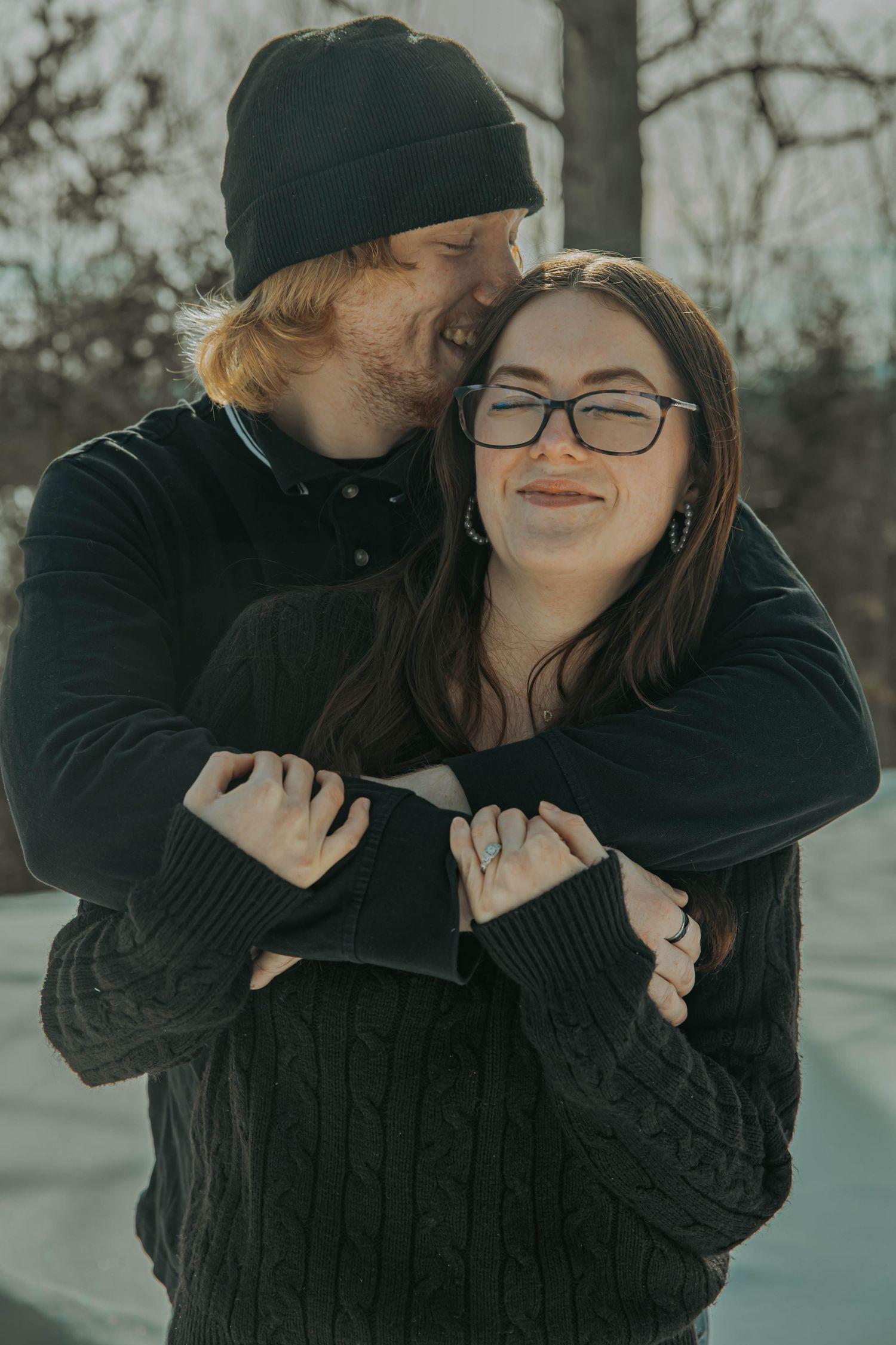 A couple in dark winter clothing share intimate moments in a snowy outdoor setting.