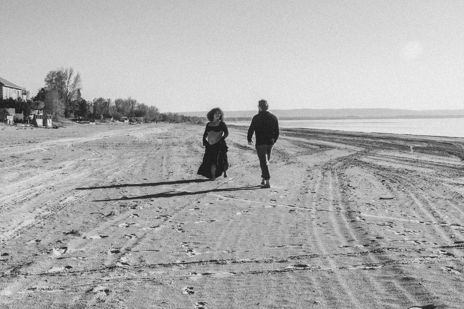 Black and white photo of two people walking along an empty beach shoreline.