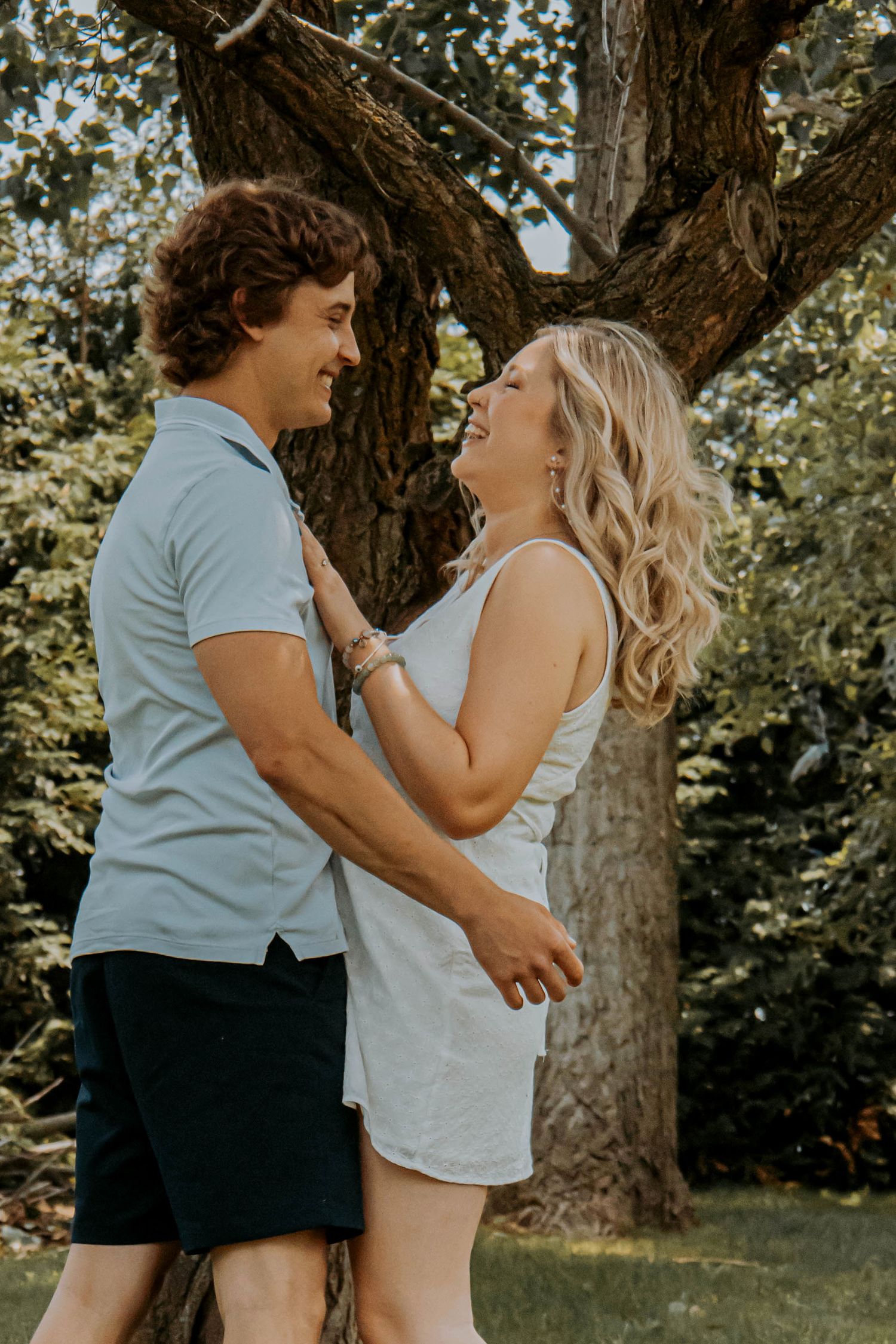 Couple sharing an intimate moment against a tree trunk in summer park setting.