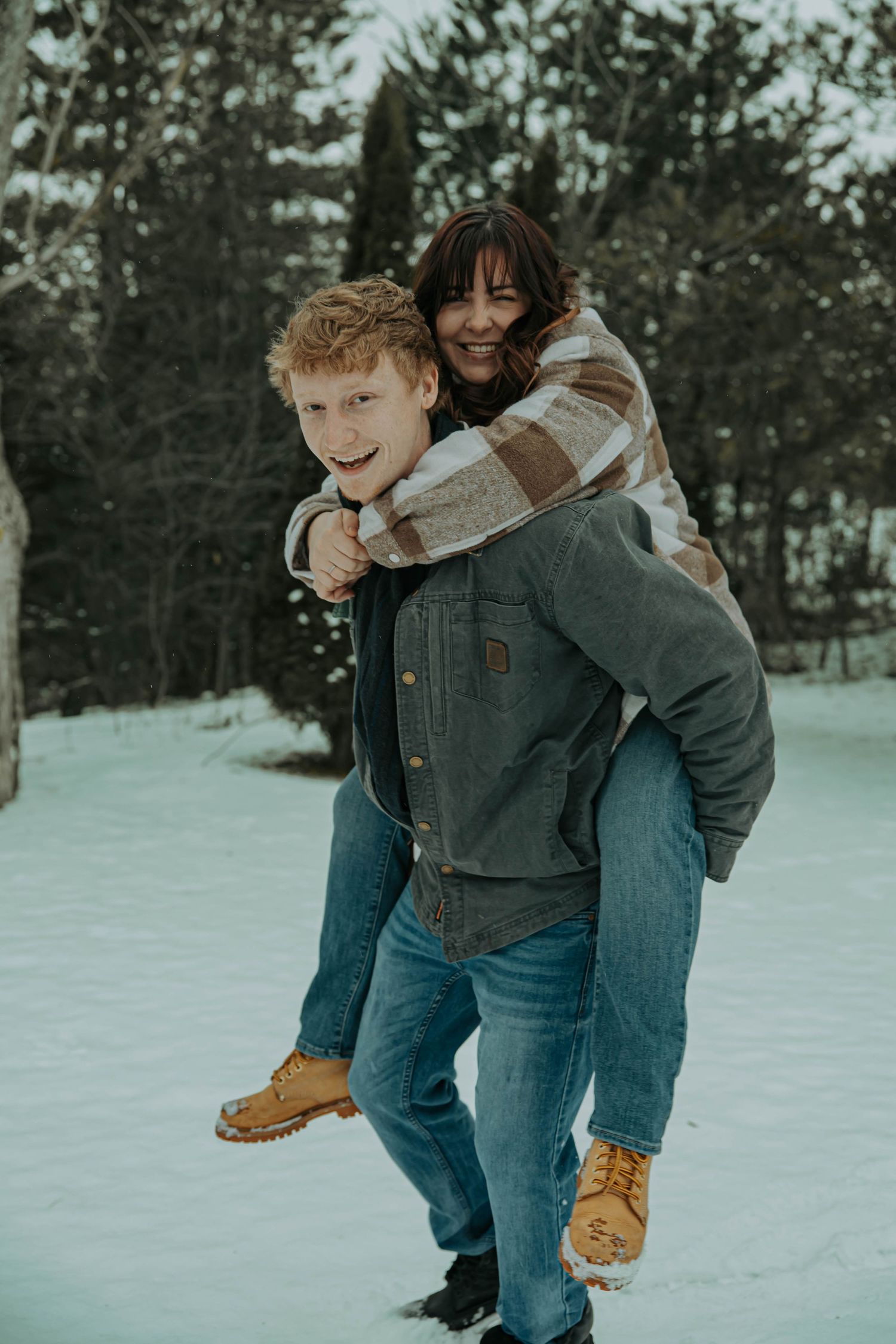 A playful couple wearing denim and winter attire share joyful moments together in the snow.