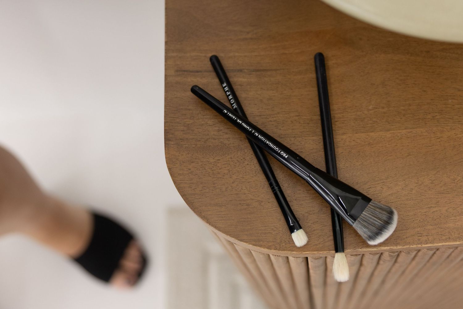 Three black makeup brushes resting on a wooden side table, perfect for professional beauty application.