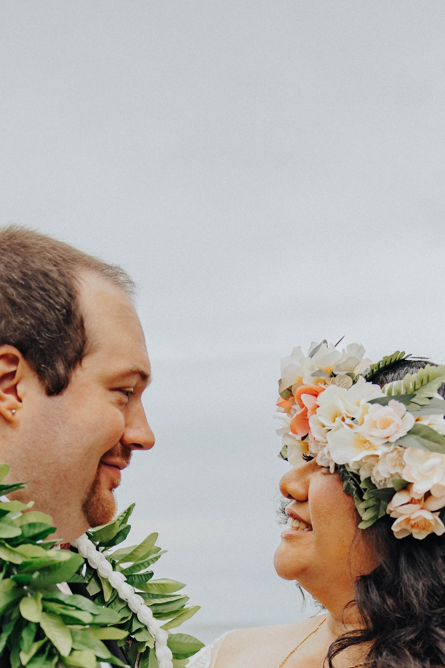 Close-up panoramic view of couple in wedding attire with peach floral arrangement against cloudy sky.