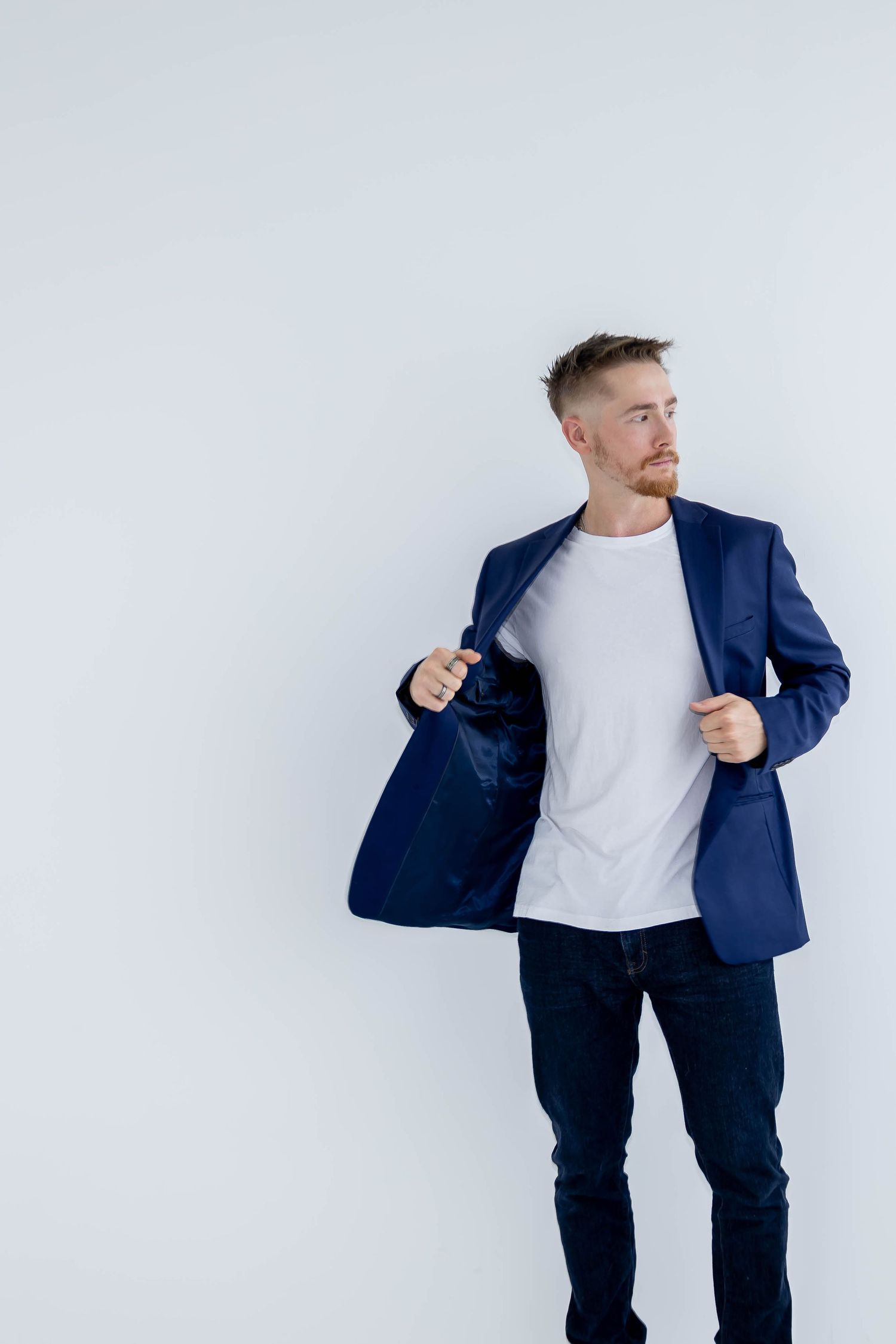 Professional wearing navy blazer and white t-shirt poses against white background in dynamic fashion series.