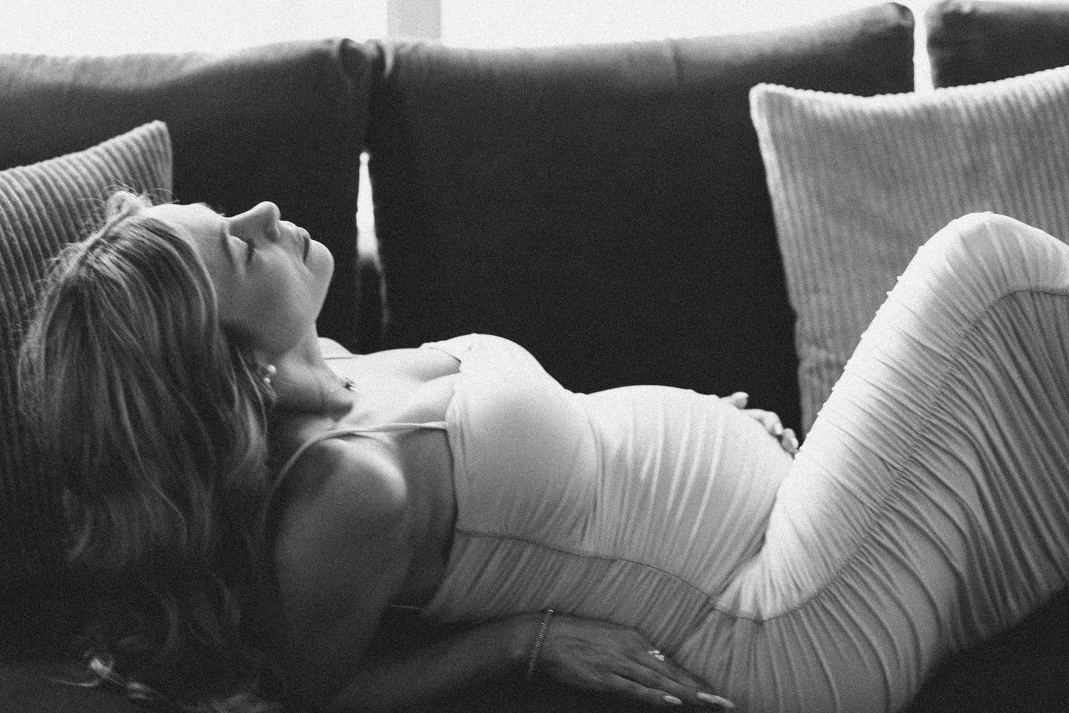 Pregnant woman relaxing on sofa in white outfit, black and white maternity photo.