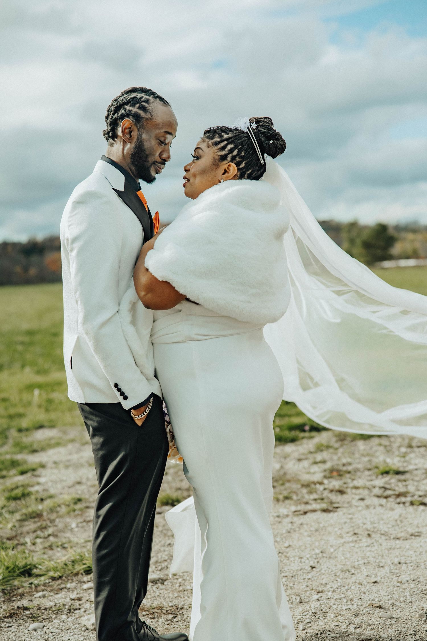 A couple shares an intimate moment outdoors as a flowing white veil catches the wind on their wedding day.