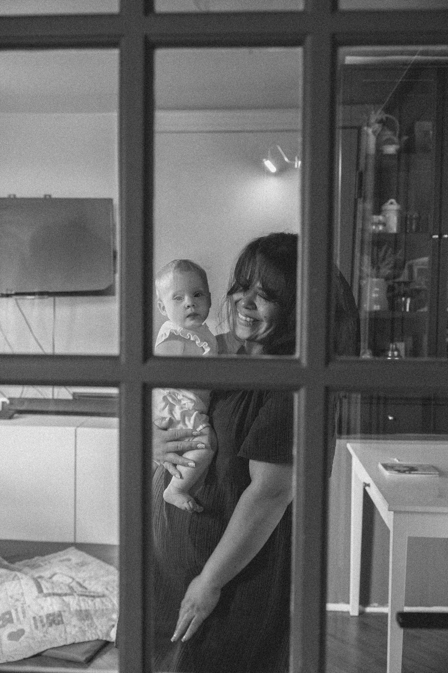 A black and white triptych photo sequence showing joyful interaction between parent and baby through a window.