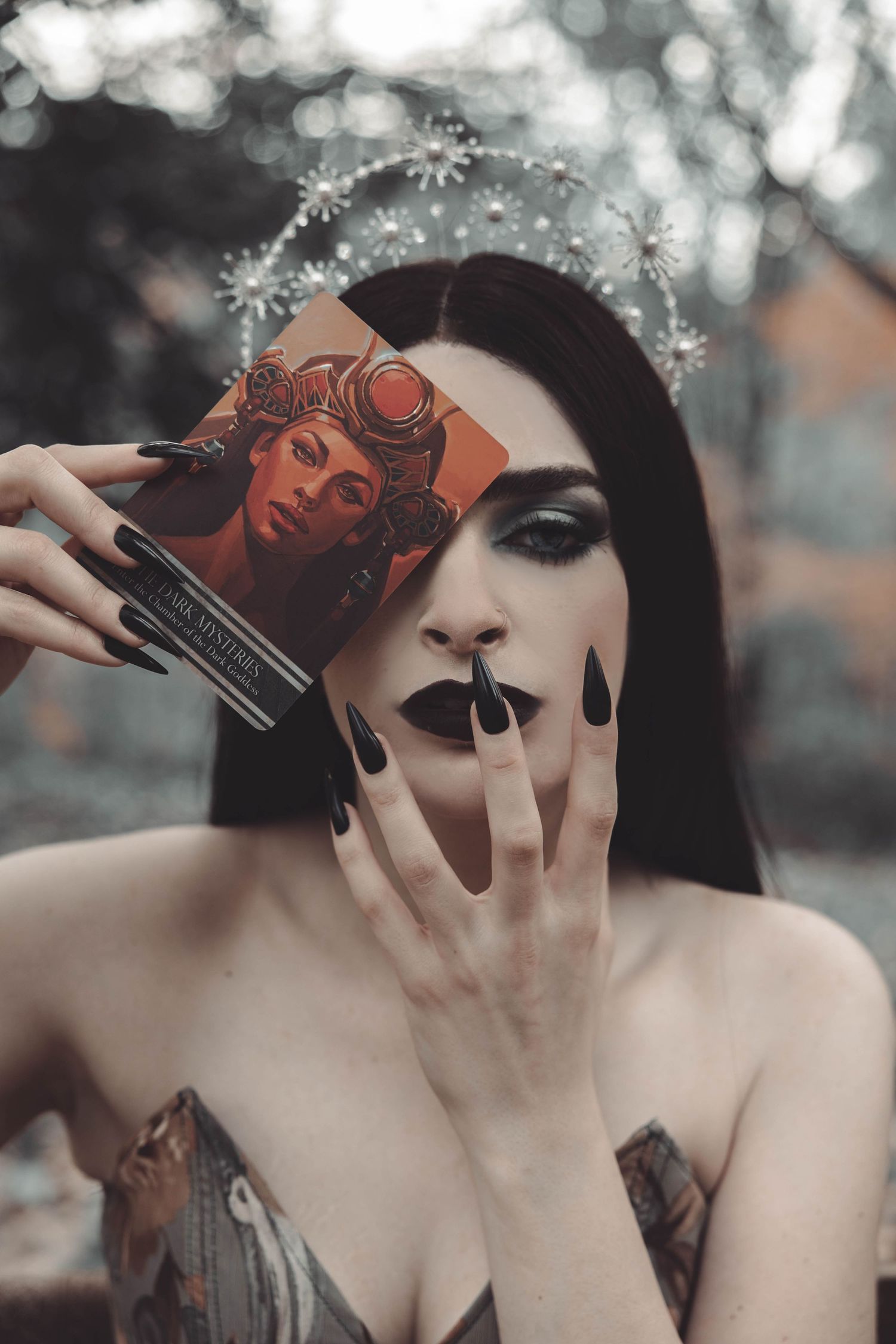 Artistic portrait showing dark gothic makeup and playing cards held near face in moody lighting.