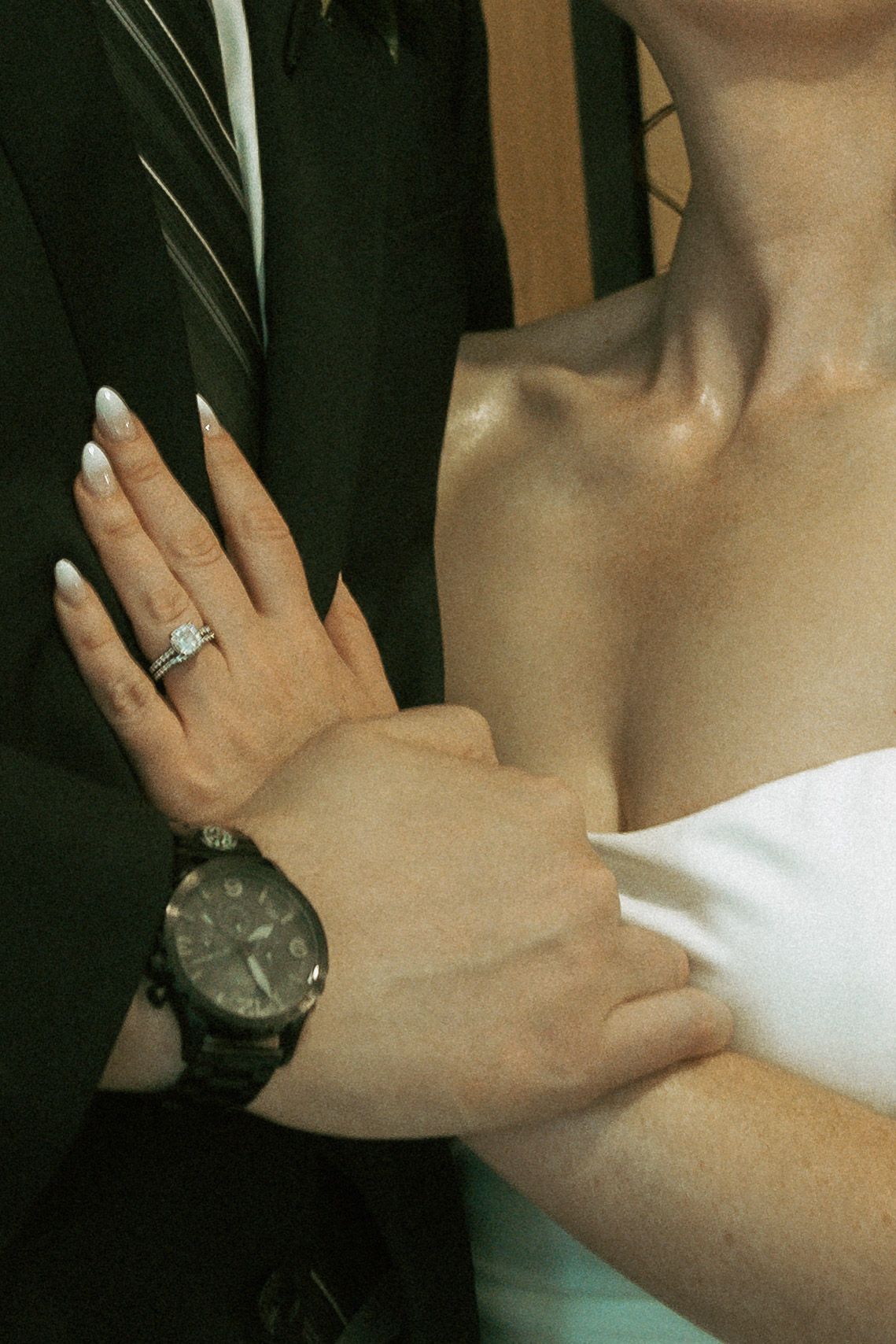 Close-up of bride and groom showing diamond engagement ring, white manicure, and black chronograph watch at wedding.