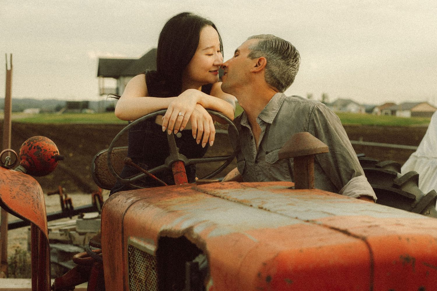Couple sharing a romantic kiss on a vintage red tractor in a rural field setting.