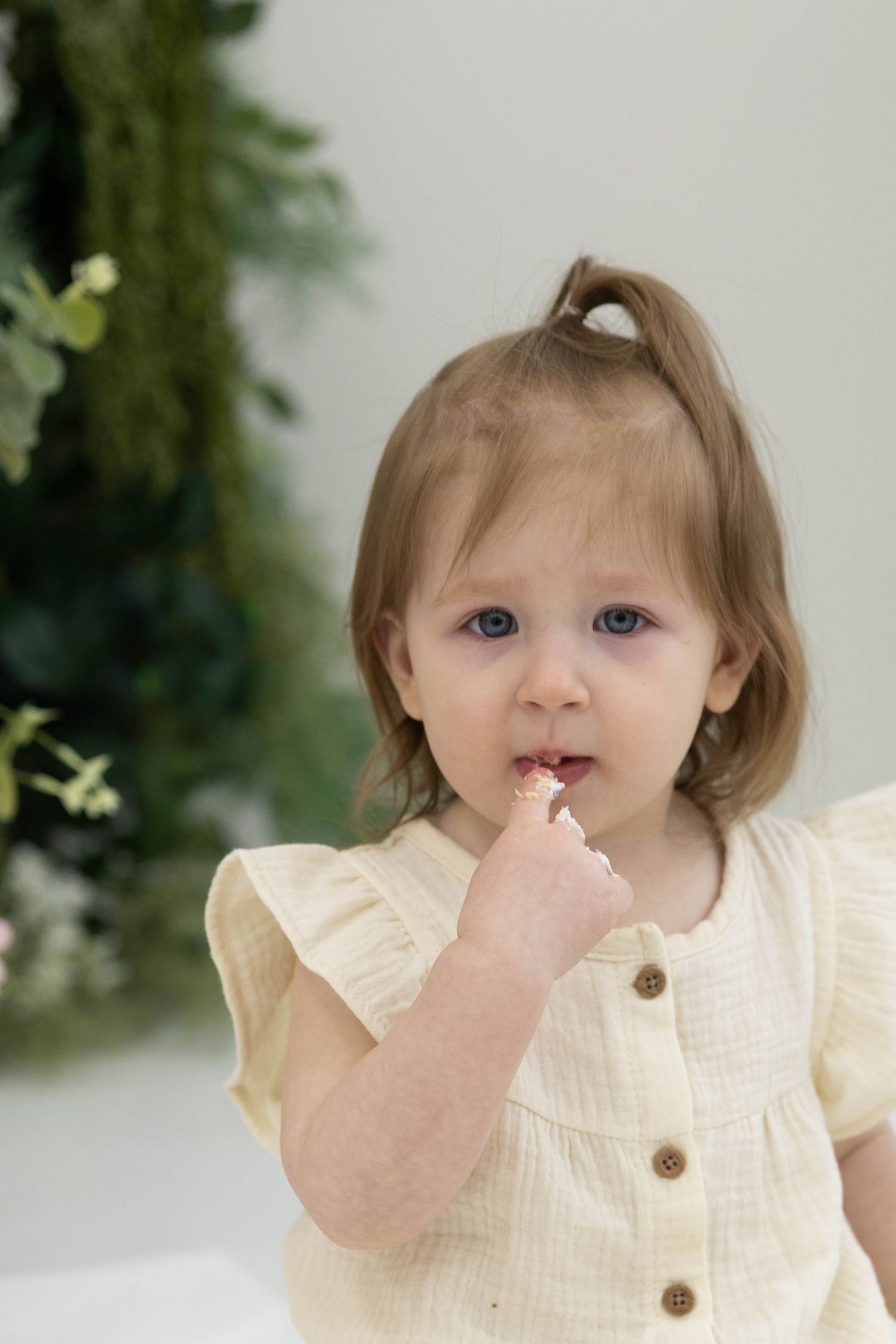 A series of four photos showing a small child in a cream-colored dress with ruffled sleeves against a soft natural background.