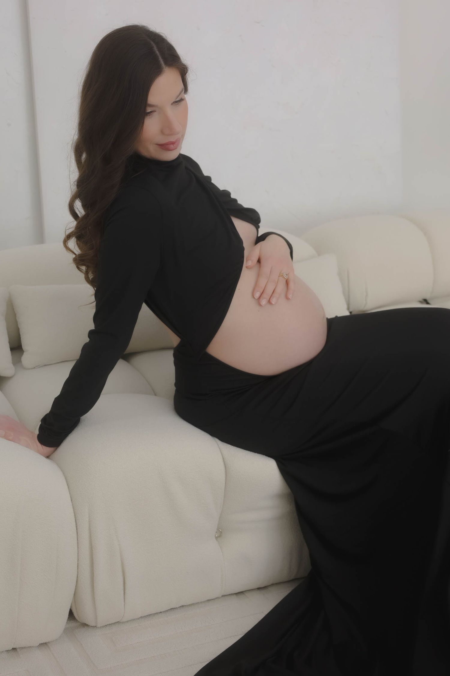 A maternity portrait on a white couch featuring a long black dress.