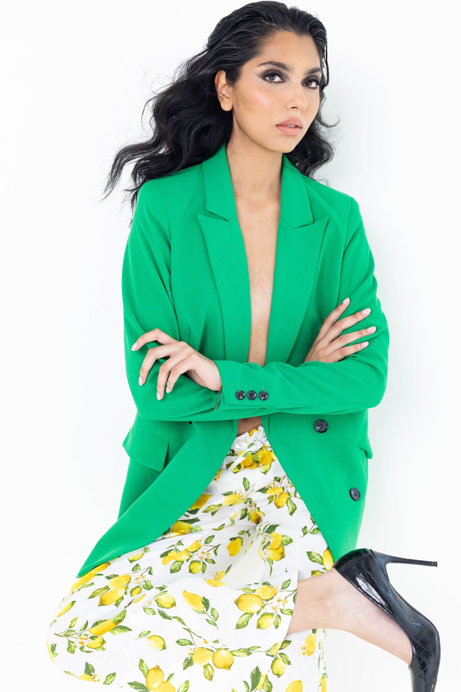 Model wearing bright green blazer and lemon print skirt with black heels in fashion photoshoot.